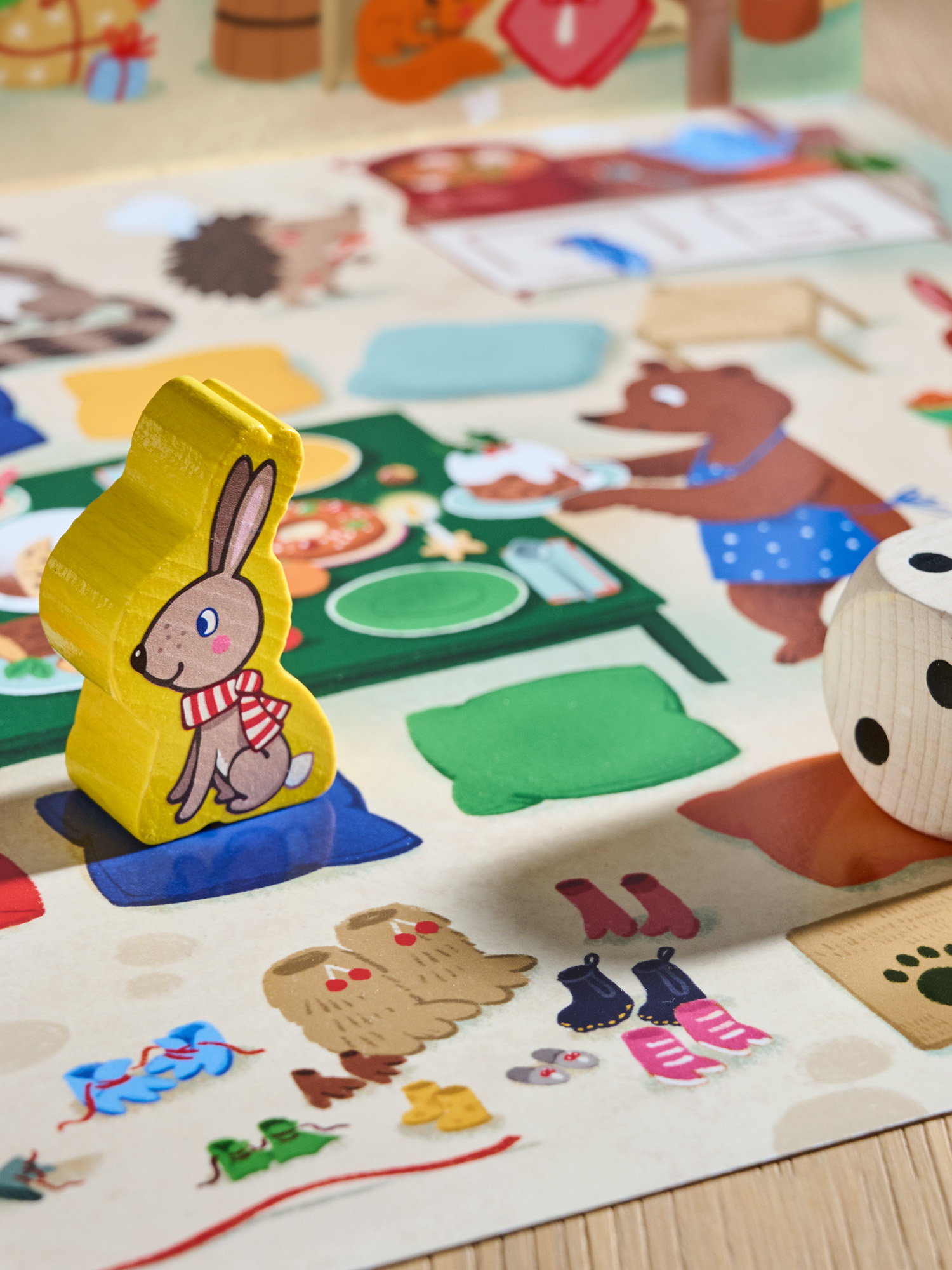 Eine gelbe Kaninchenfigur mit Schal sitzt auf einem Brettspiel. Ein Bär serviert Essen. Würfel und andere Spielsteine sind in der Nähe.