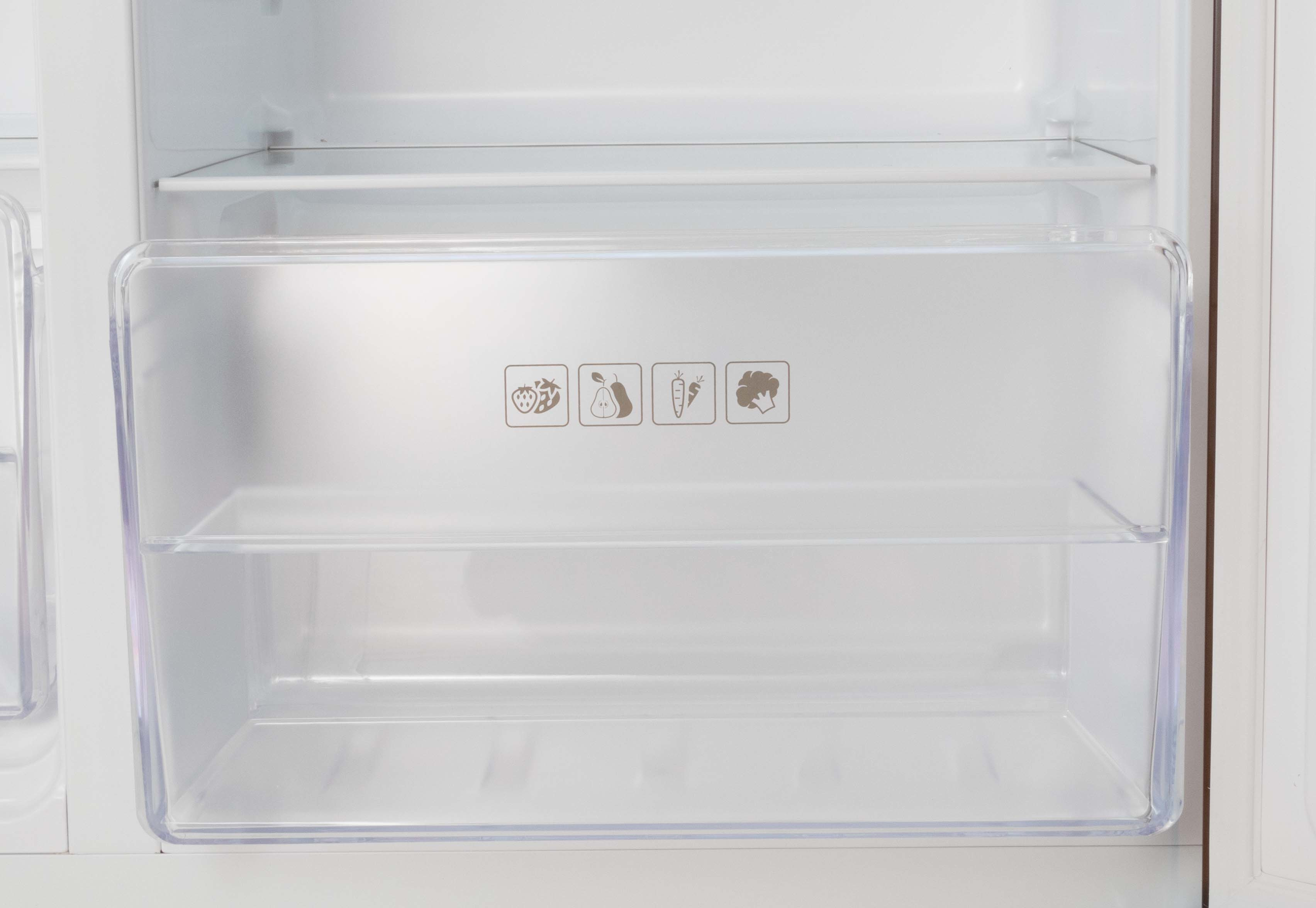An empty refrigerator with a clear vegetable bin. Fruit and vegetable icons are on the front.