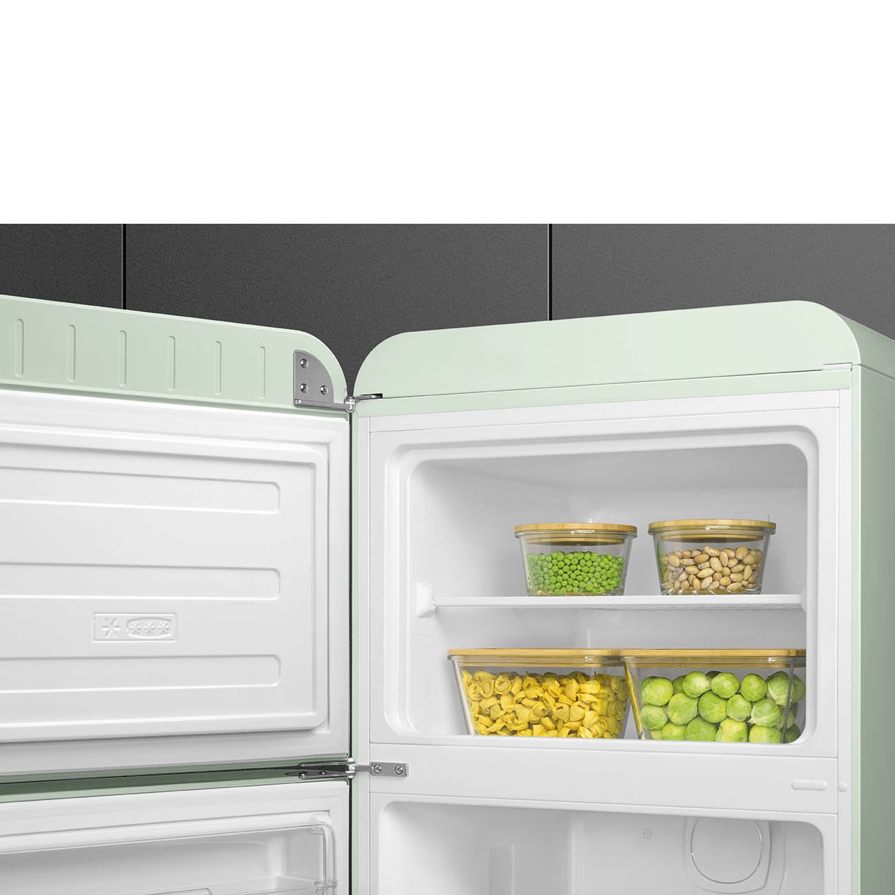 Un refrigerador abierto de estilo retro. En el interior, recipientes de vidrio contienen guisantes, frijoles, pasta y coles de Bruselas. La puerta del congelador está abierta.