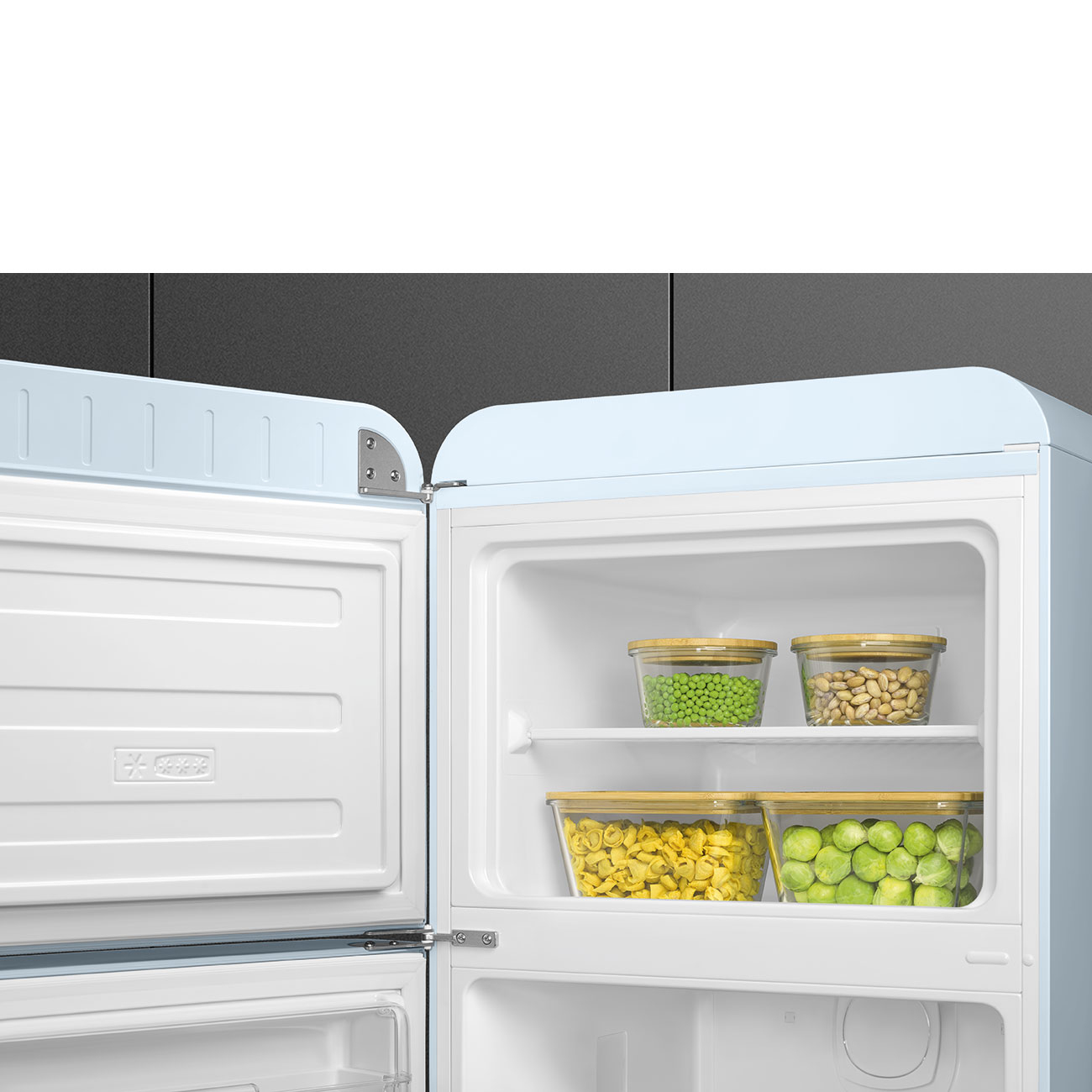 Un refrigerador azul claro abierto. El congelador está a la izquierda. Los estantes contienen recipientes con guisantes, frijoles, pasta y coles de Bruselas.