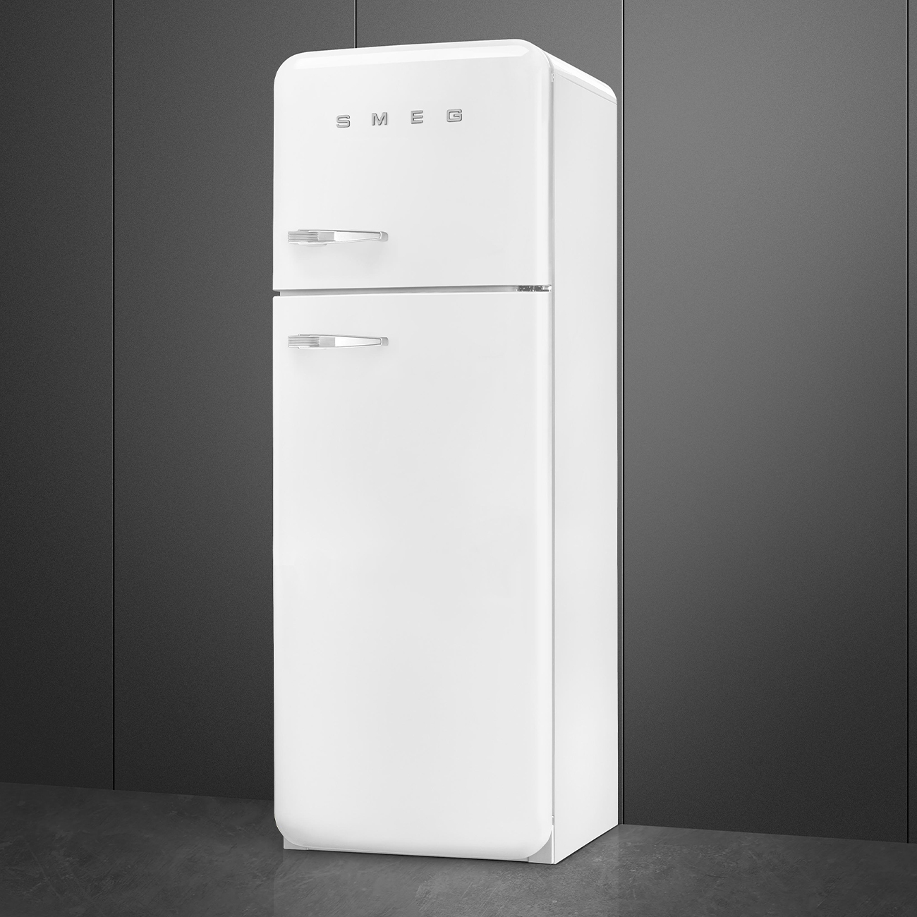 Un refrigerador Smeg blanco se alza contra una pared gris oscura. Tiene dos puertas y manijas cromadas. 'SMEG' impreso arriba.