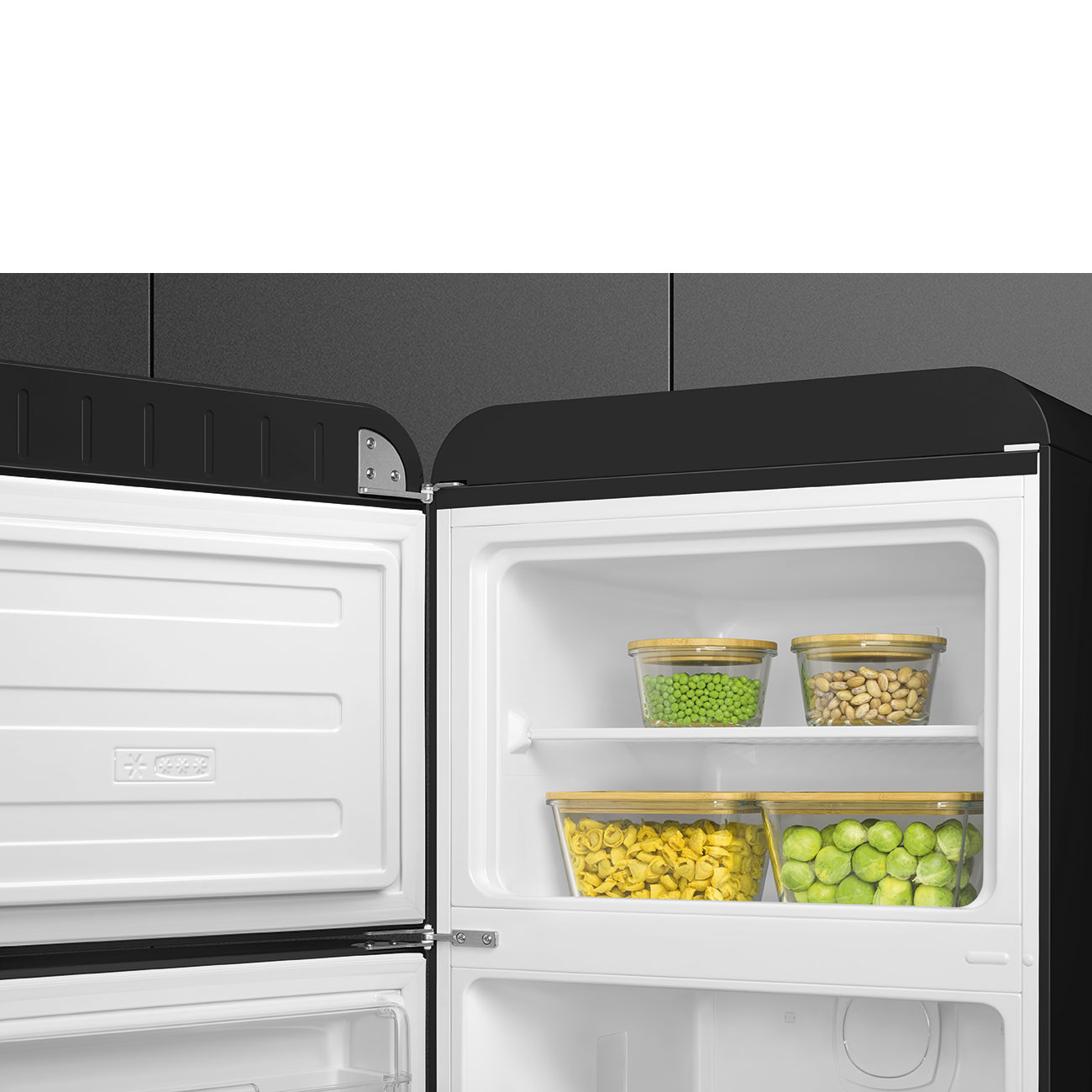 Offener Kühlschrank mit Behältern mit Erbsen, Nüssen, Tortellini und Rosenkohl. Der Kühlschrank ist schwarz und weiß.