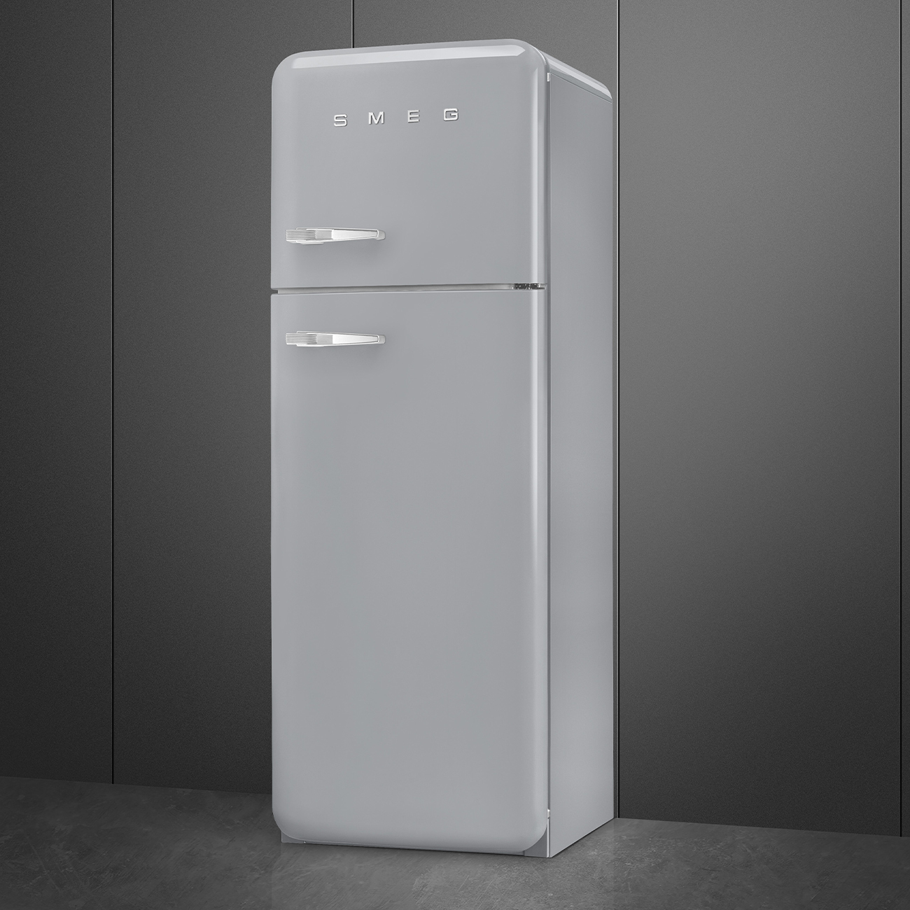 Un refrigerador SMEG gris claro se encuentra contra una pared gris oscuro. El refrigerador tiene un diseño retro con manijas cromadas.
