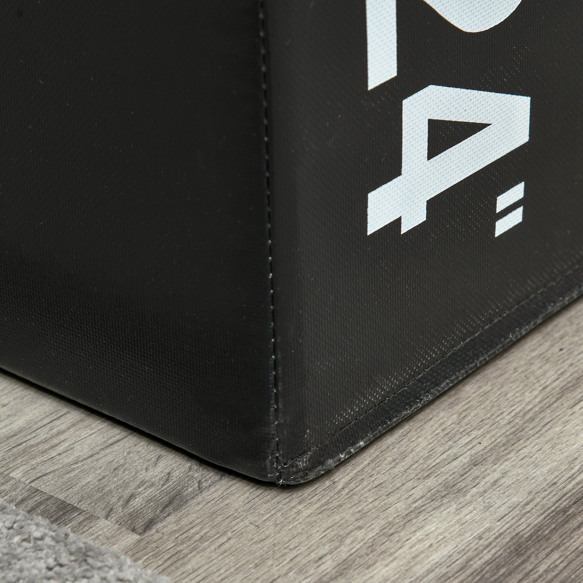 Esquina de caja negra con texto blanco sobre suelo de madera gris, primer plano.