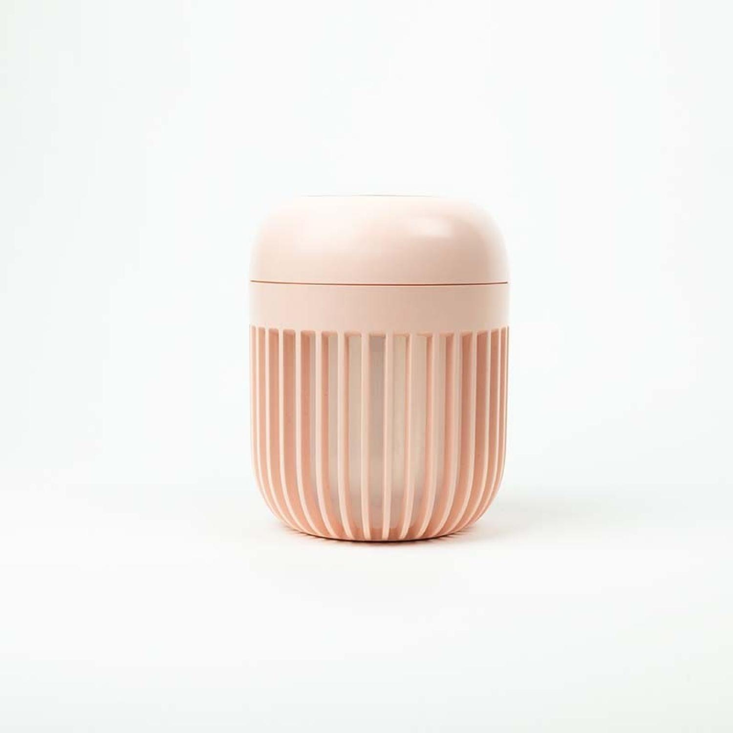 Un recipiente rosa claro con la mitad inferior acanalada y la parte superior lisa y redondeada sobre fondo blanco.