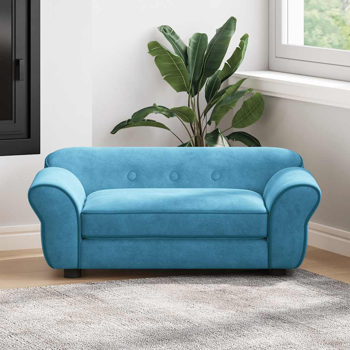 Ein blaues Sofa mit abgerundeten Armlehnen steht in einem Raum. Dahinter befindet sich eine große Pflanze. Rechts ist ein Fenster. Der Boden ist aus Holz.