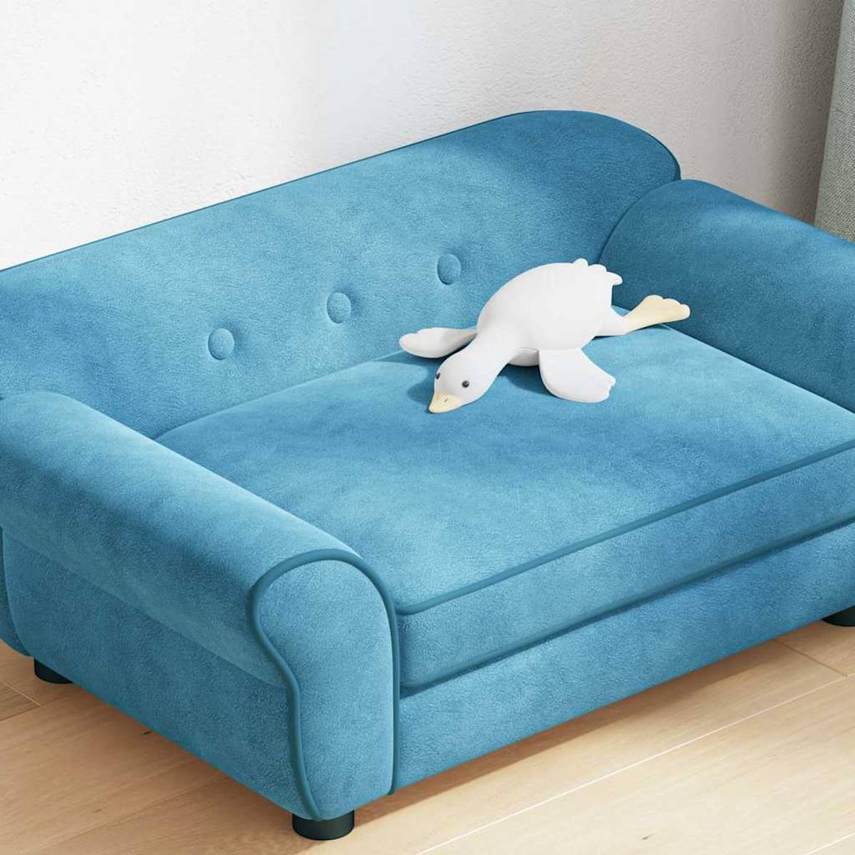 Ein blaues Kindersofa mit einem weißen Entenspielzeug darauf. Das Sofa hat eine geknöpfte Rückenlehne und steht auf Holzboden.