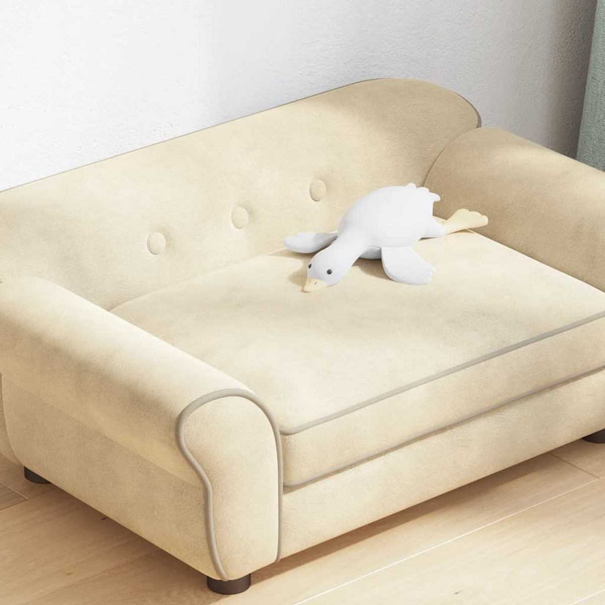 Ein kleines beiges Sofa mit einem weißen Enten-Plüschtier. Das Sofa hat Knöpfe und eine graue Umrandung. Die Ente liegt auf dem Kissen.