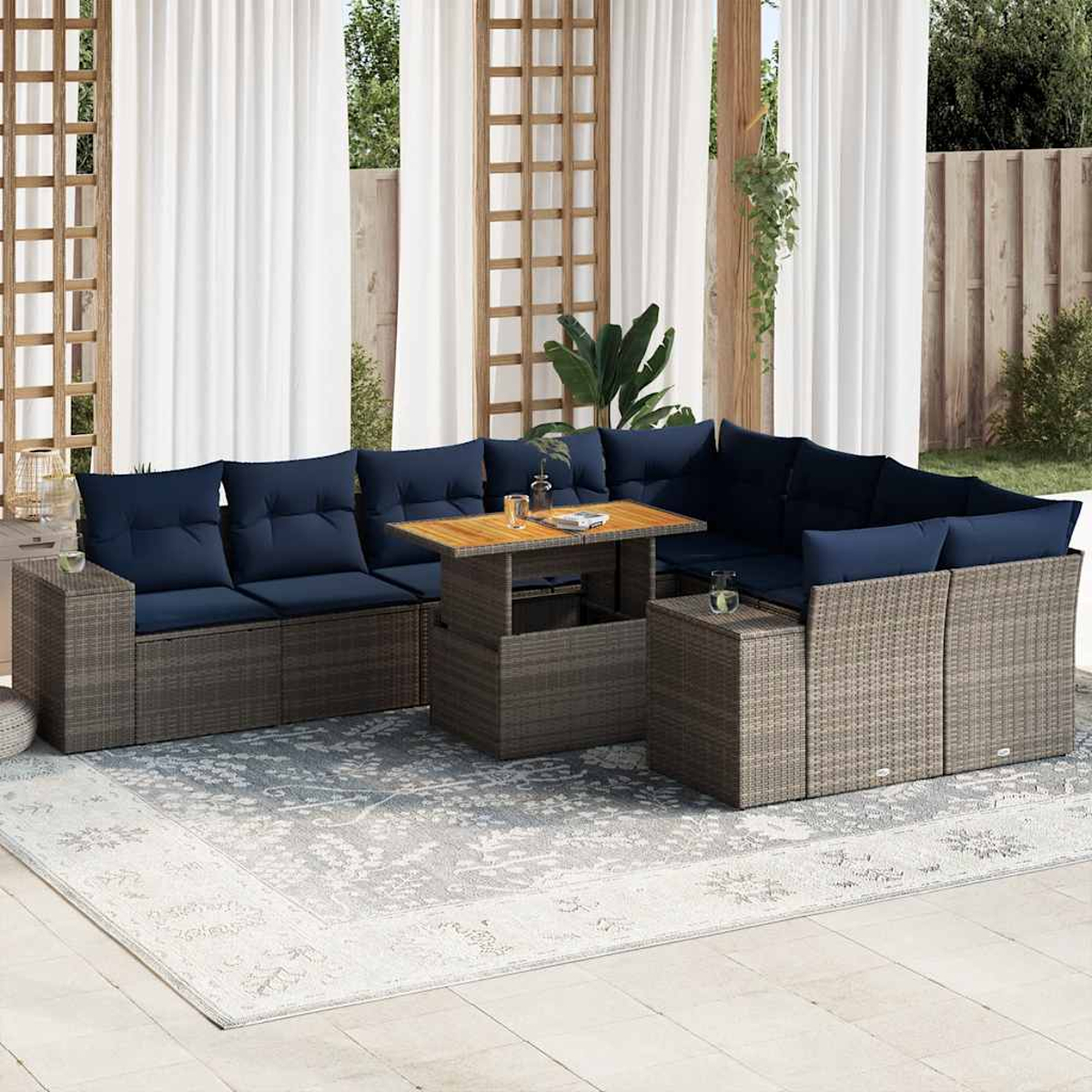 Sofá seccional para exteriores con cojines azul marino y una mesa de madera sobre una alfombra estampada, en un patio con cortinas blancas.