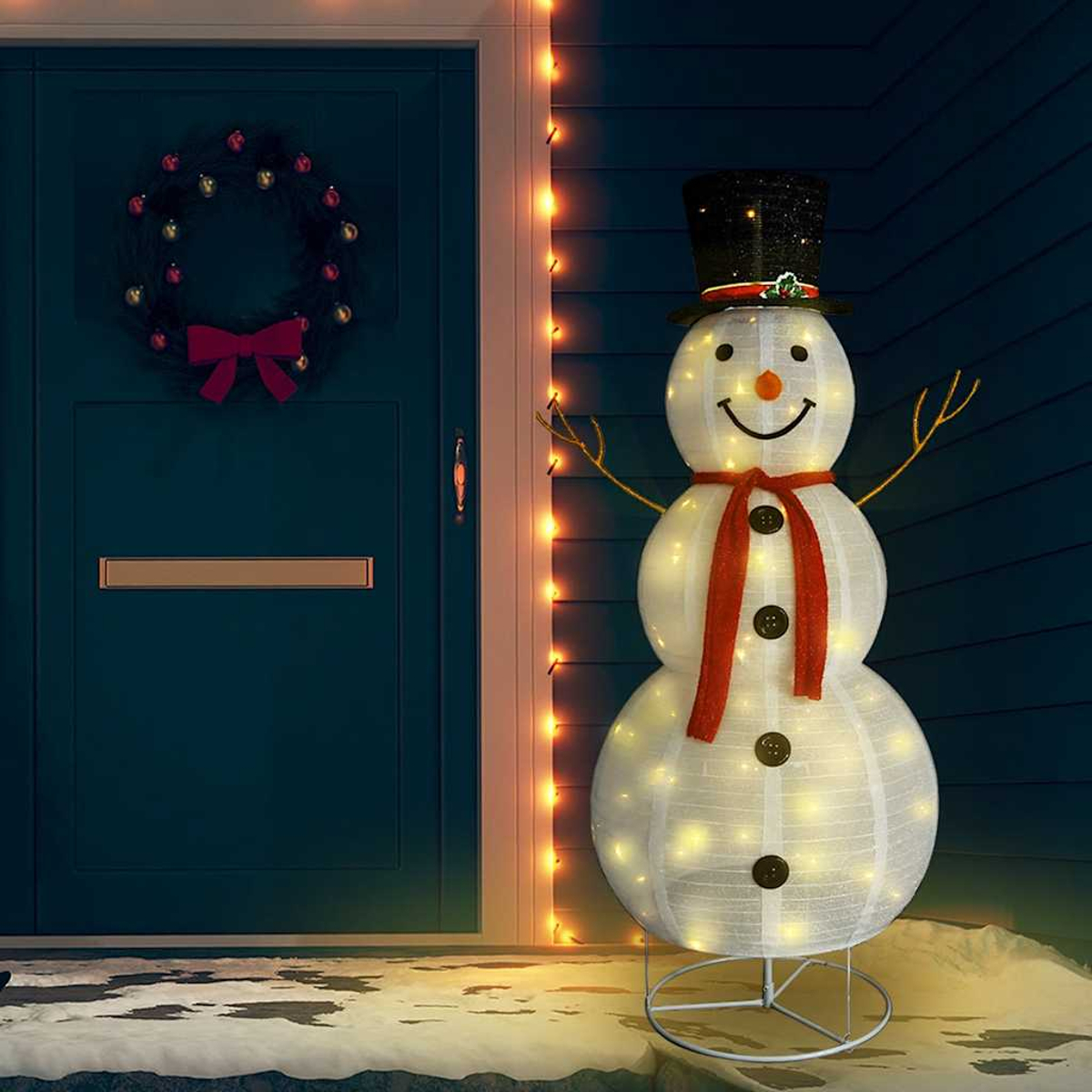Ein Schneemann mit Hut, Schal und Knöpfen steht neben einer Tür mit Kranz. Lichterketten und eine rote Schleife ergänzen die festliche Szene.