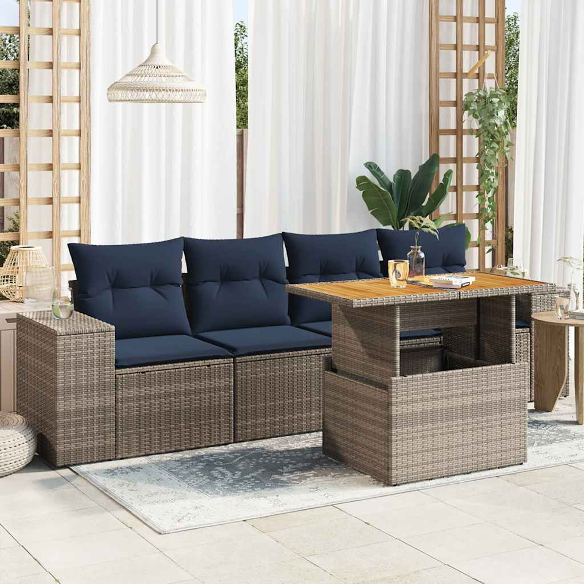 Asientos al aire libre con cojines azules y una mesa de madera. Se ven cortinas, plantas y muebles tejidos, creando un ambiente de patio.