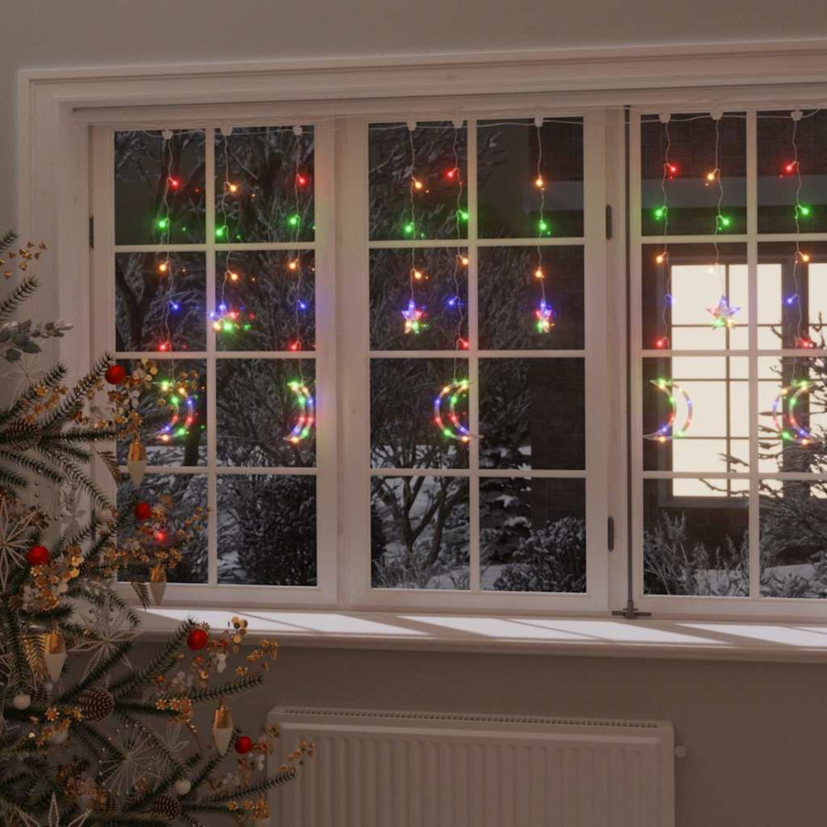 Ein Fenster mit Weihnachtsbeleuchtung in Form von Sternen und Monden. Draußen ist eine schneebedeckte Szene zu sehen. Links ist ein Weihnachtsbaum.