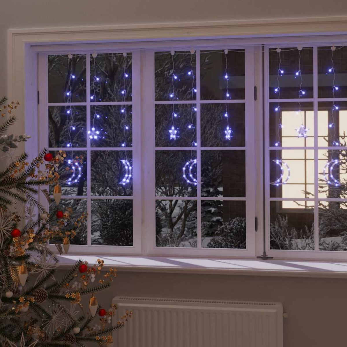 Ein Fenster mit Weihnachtsbeleuchtung in Form von Monden und Sternen. Ein geschmückter Weihnachtsbaum steht links, draußen ist Schnee zu sehen.