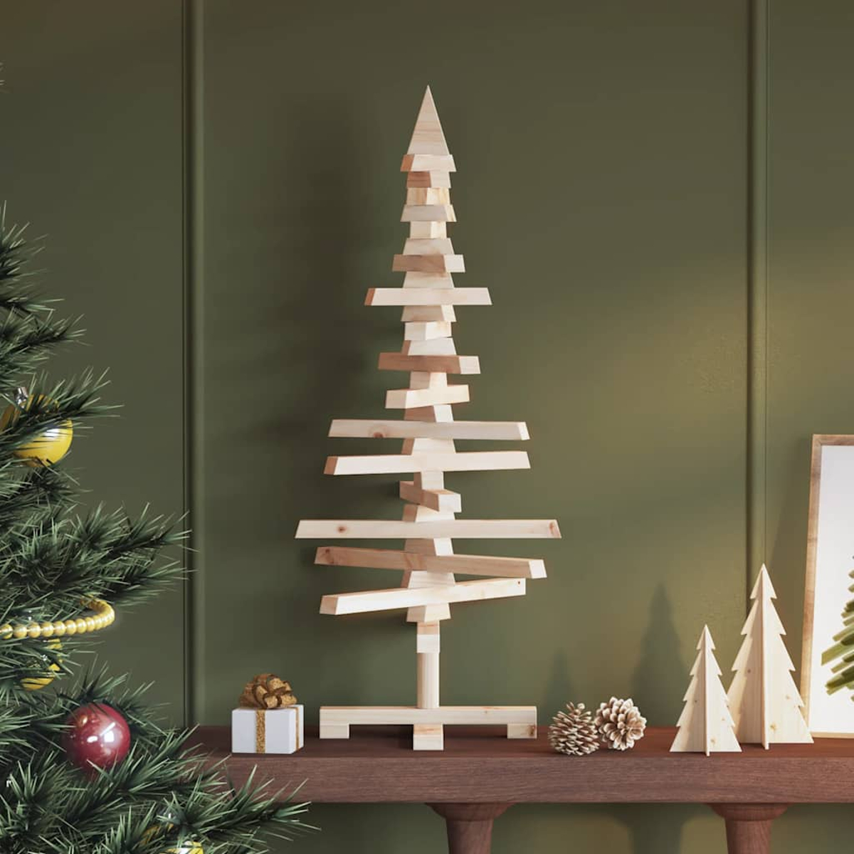 Ein Weihnachtsbaum aus Holzbrettern steht auf einem braunen Tisch. Dekorationen sind ein Geschenk, Tannenzapfen und kleine Holzbäume.