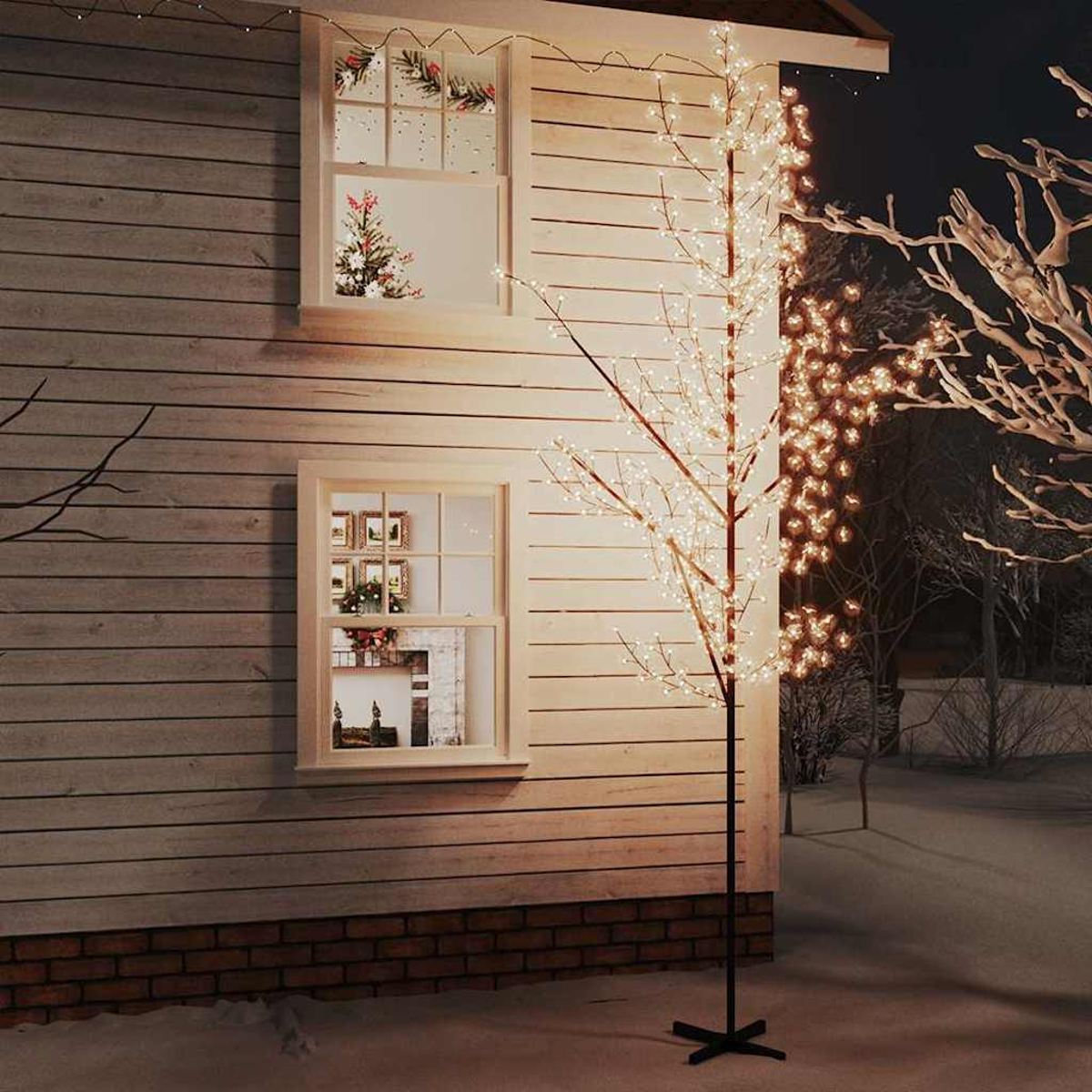 Ein Haus mit beleuchteten Fenstern und einem dekorativen Baum. Ein mit Licht bedeckter Baum steht vor dem Haus. Schnee bedeckt den Boden.