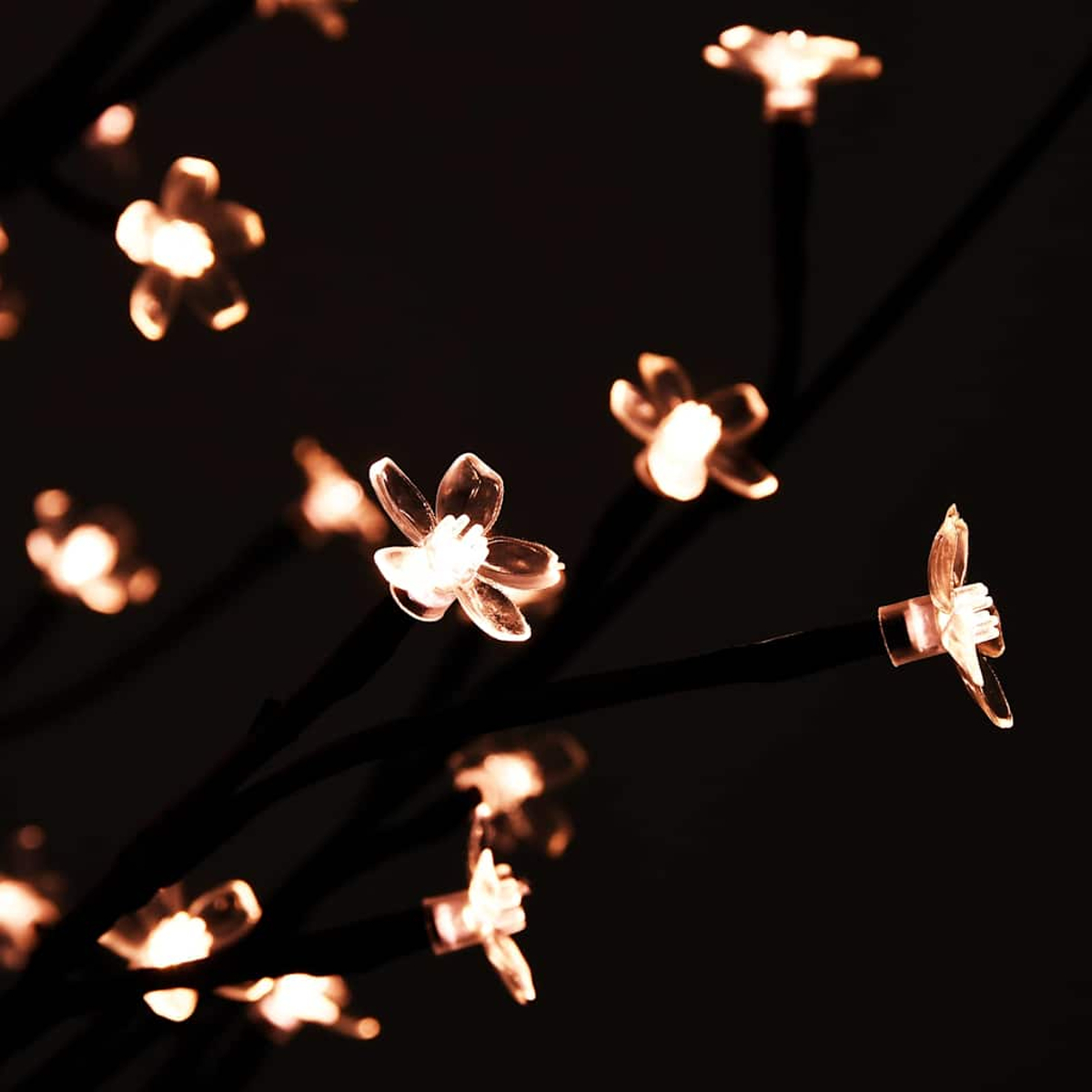 Nahaufnahme eines dekorativen Baumes mit leuchtenden blütenförmigen Lichtern vor dunklem Hintergrund. Die Lichter sind warm und die Äste schwarz.