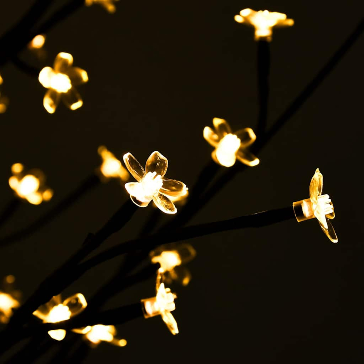 Nahaufnahme von dekorativen Baumzweigen mit leuchtenden, blütenförmigen Lichtern. Dunkler Hintergrund. Lichter sind gelb und die Äste sind schwarz.