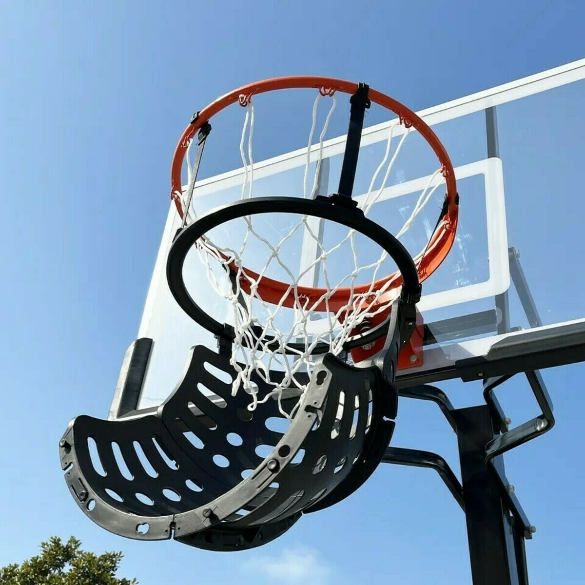A basketball hoop with an orange rim and white net. A black backboard and a clear plastic backboard sit against a blue sky.