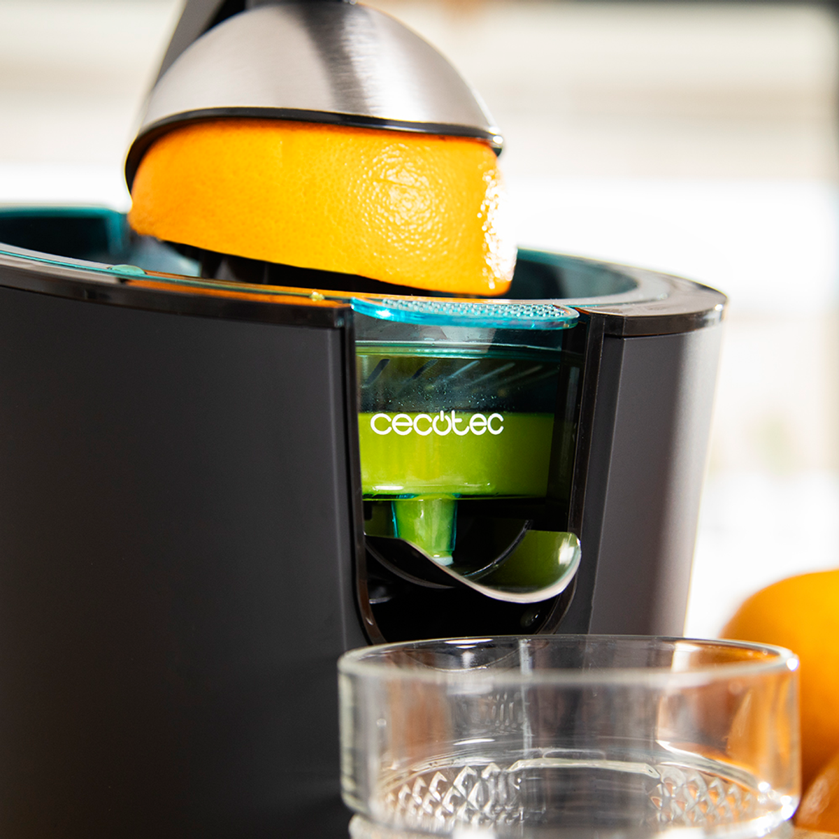 Eine Saftpresse mit einer ausgepressten Orange. Frisch gepresster Saft im Behälter, ein Glas davor. Schwarze und silberne Saftpresse.