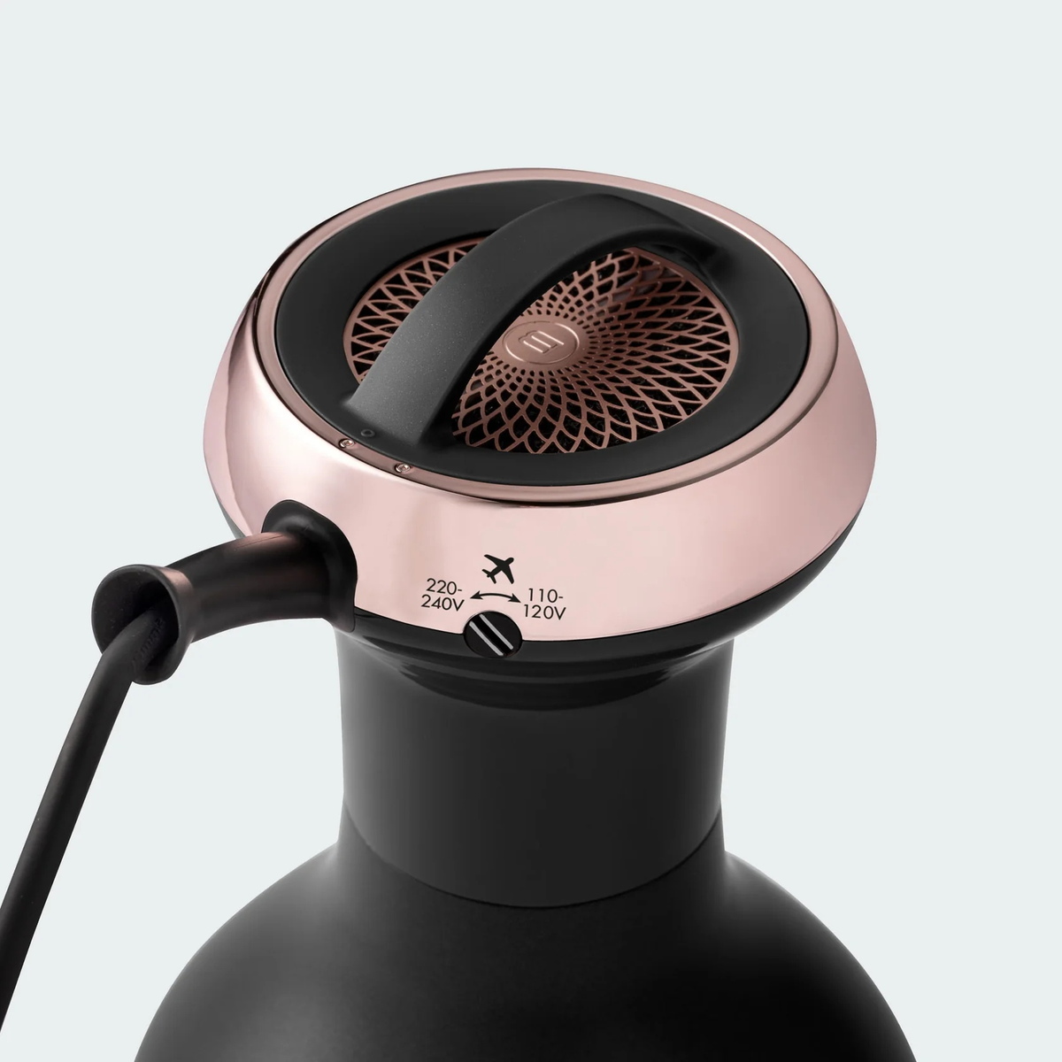 Zbliżenie czarnej i różowo-złotej suszarki do włosów. Zawiera uchwyt, siatkowy wierzch i selektor napięcia.