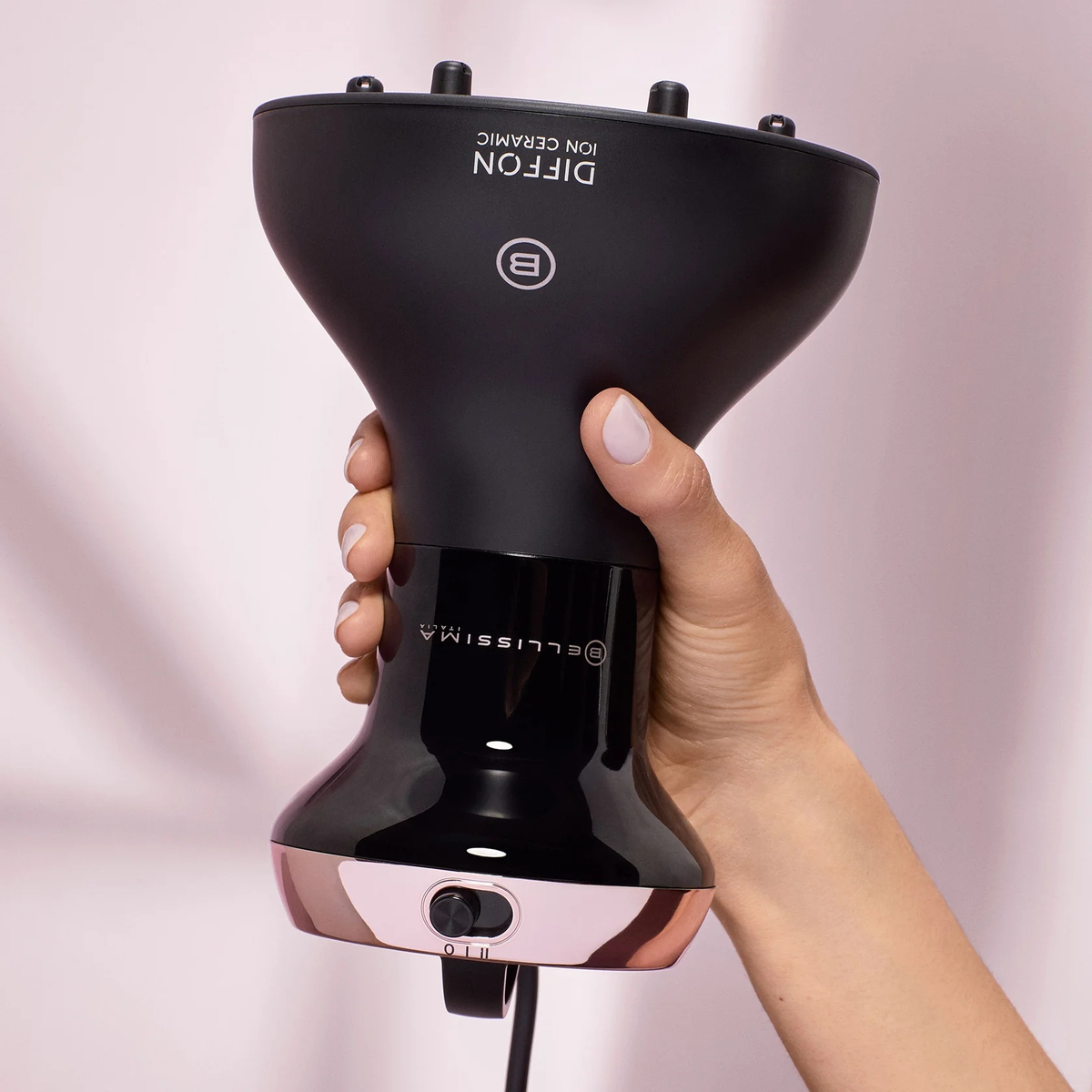 Dłoń trzyma czarny i różowo-złoty dyfuzor do włosów. Nazwa marki i model są widoczne na urządzeniu.