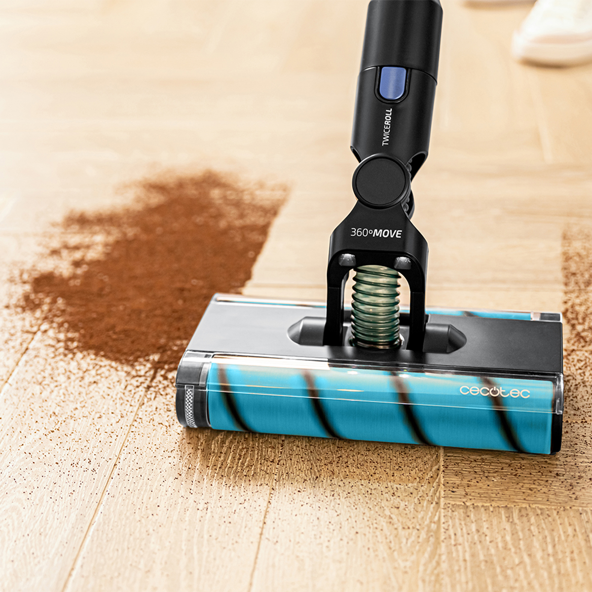 Una aspiradora limpia restos marrones en un suelo de madera. La aspiradora tiene un mango negro y un rodillo azul y negro.