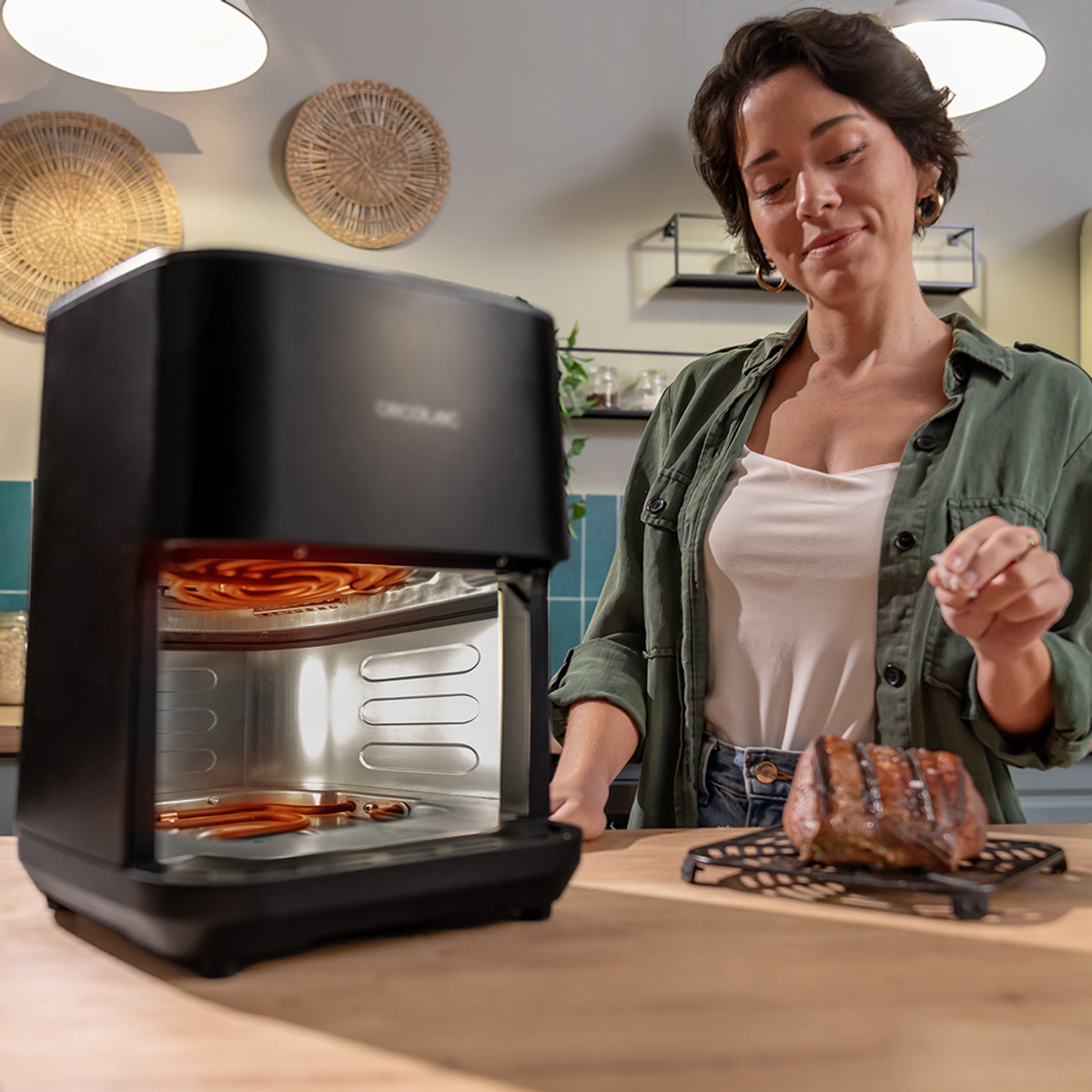 Kobieta w kuchni z frytownicą powietrzną i gotowanym mięsem. Uśmiecha się. Kuchnia ma oświetlenie i dekoracje ścienne.