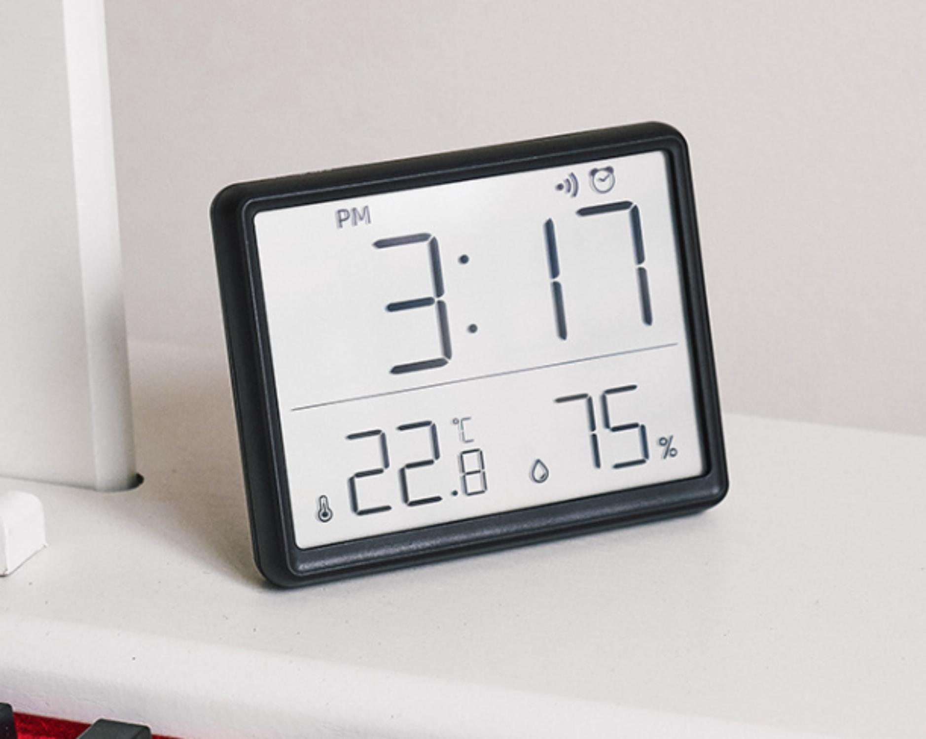 Eine Digitaluhr zeigt 15:17 Uhr, 22,8°C und 75% Luftfeuchtigkeit an. Die Uhr hat einen schwarzen Rahmen auf weißem Untergrund.