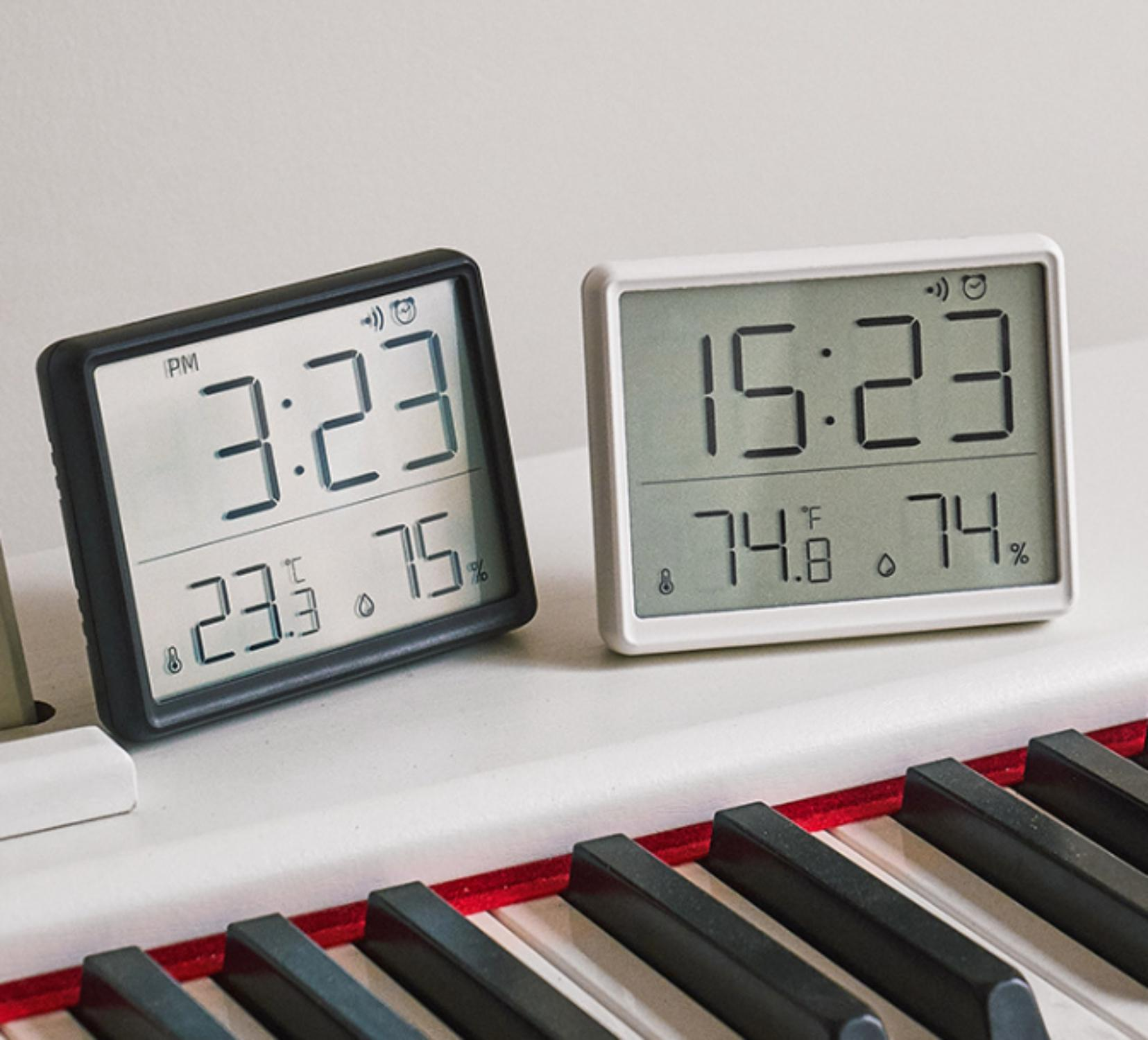 Zwei Digitaluhren auf einem Klavier. Eine zeigt 15:23 Uhr, 23,3 Grad und 75 %. Die andere zeigt 15:23 Uhr, 74,8 Grad und 74 %.