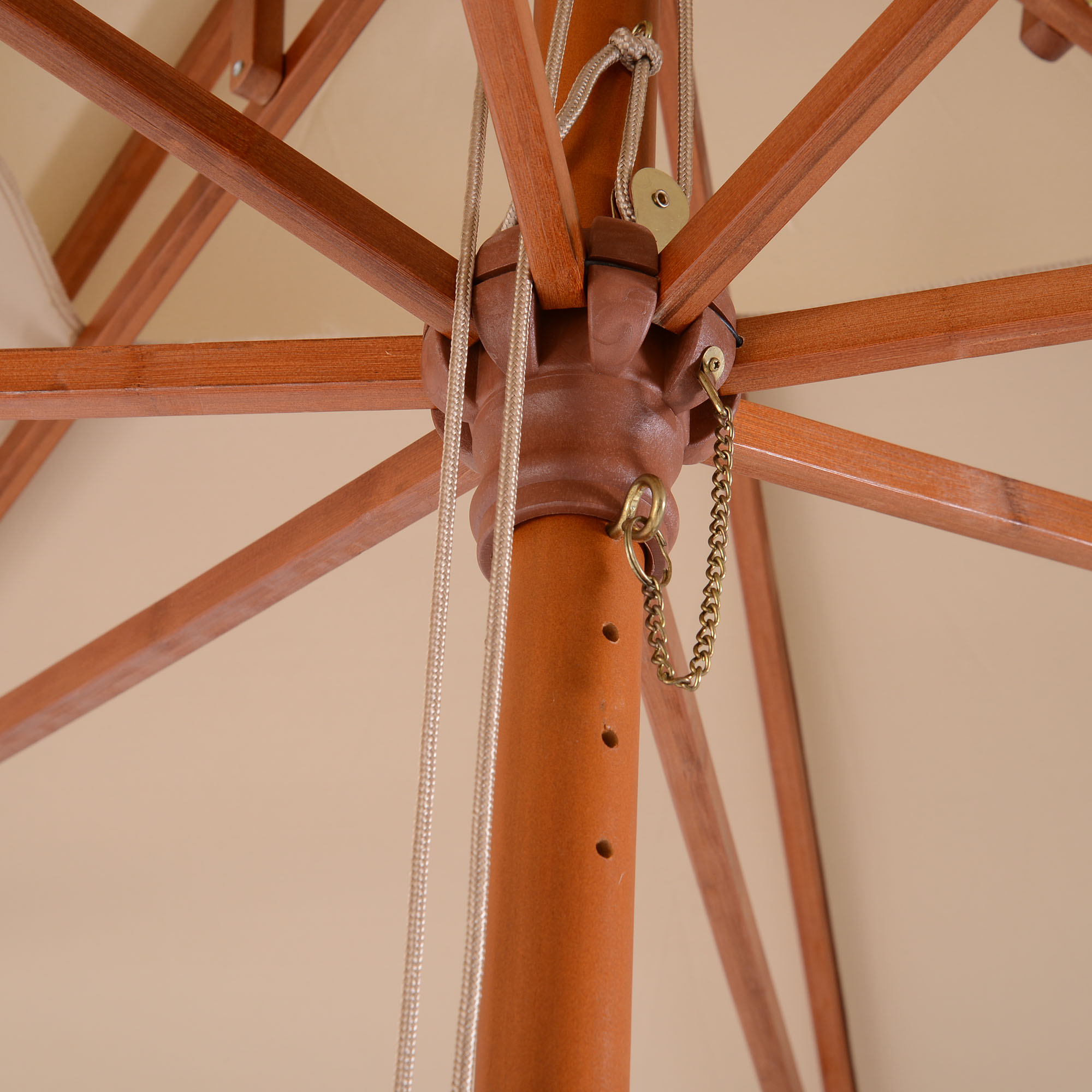 Primo piano della struttura di un ombrellone in legno aperto, la capote beige e il palo centrale con corde e catena.