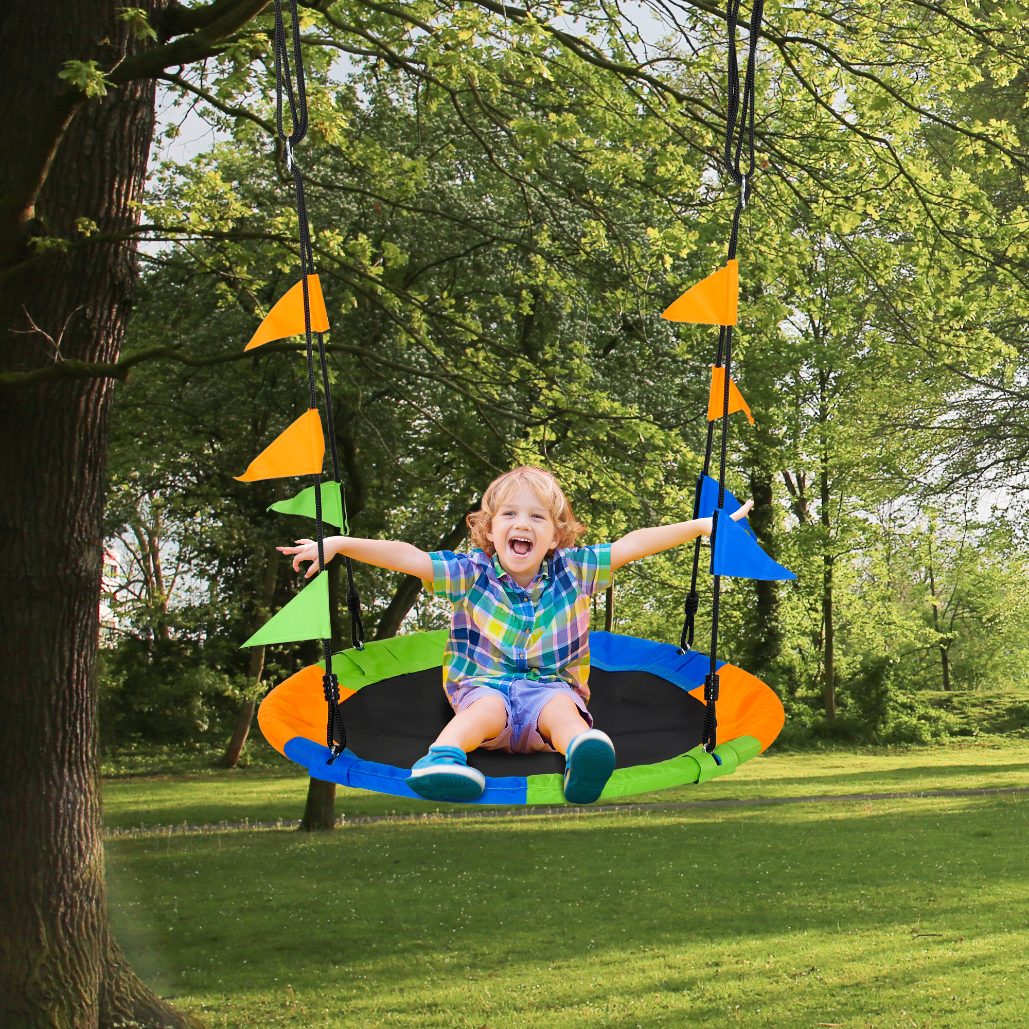 Un niño se balancea en un columpio de árbol en un parque. El columpio es colorido con banderas.