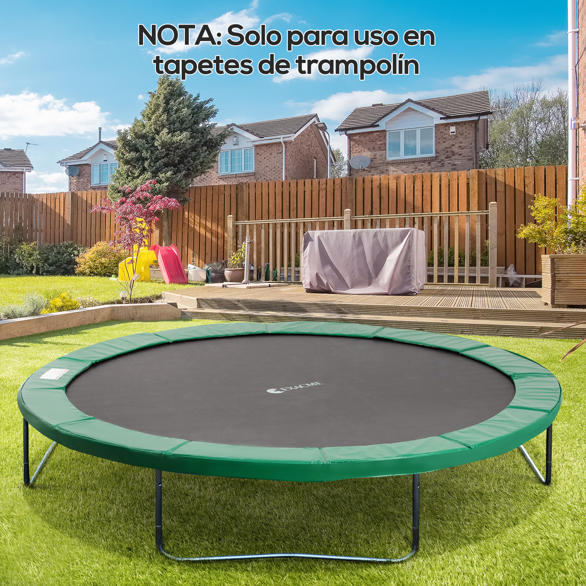 Un trampolín verde se encuentra en un césped verde. Al fondo hay casas, una terraza de madera y un cielo azul.