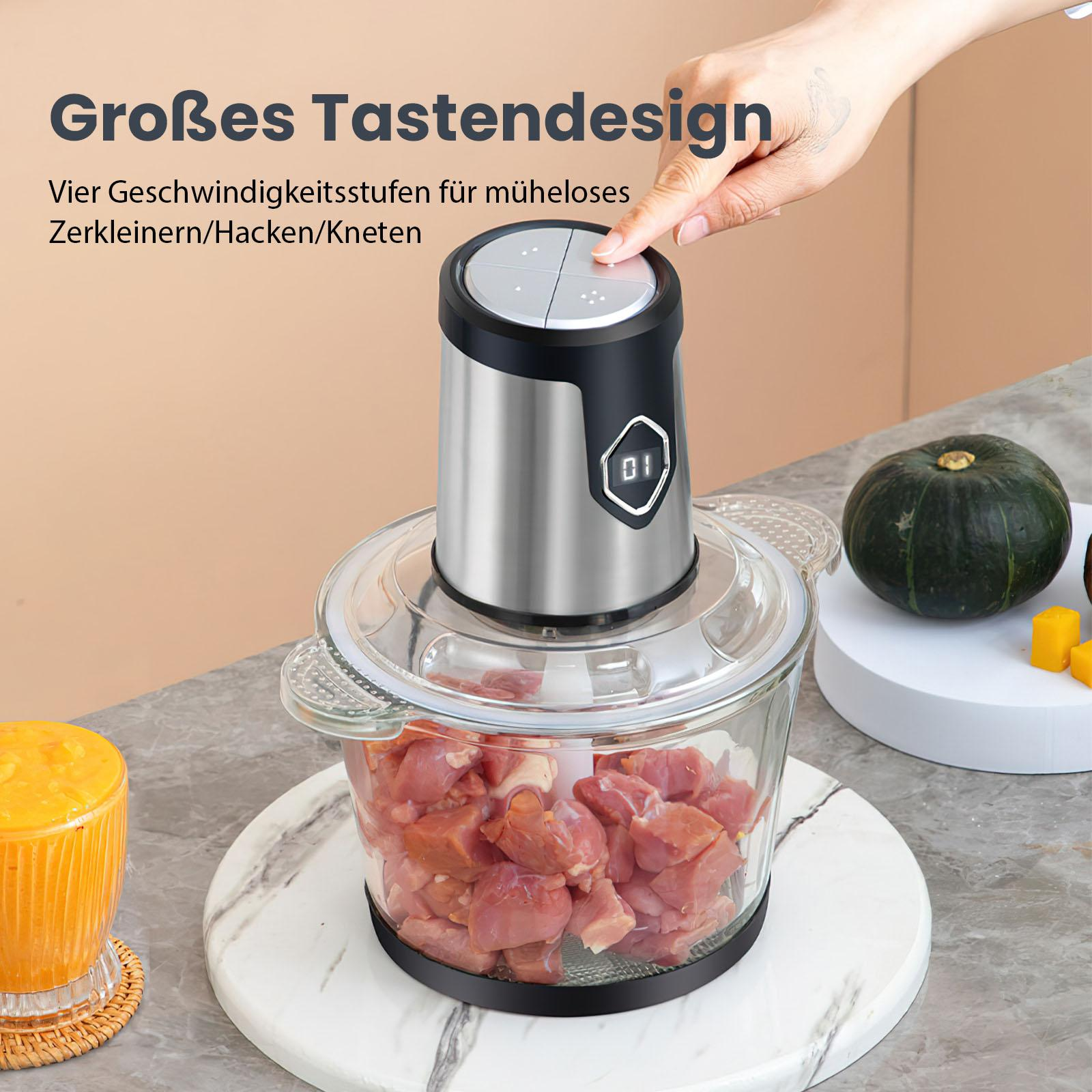 Eine Hand drückt einen Knopf an einem silbernen Foodprozessor. Eine Glasschüssel ist mit Fleisch gefüllt. Kürbis und Saft sind vorhanden.