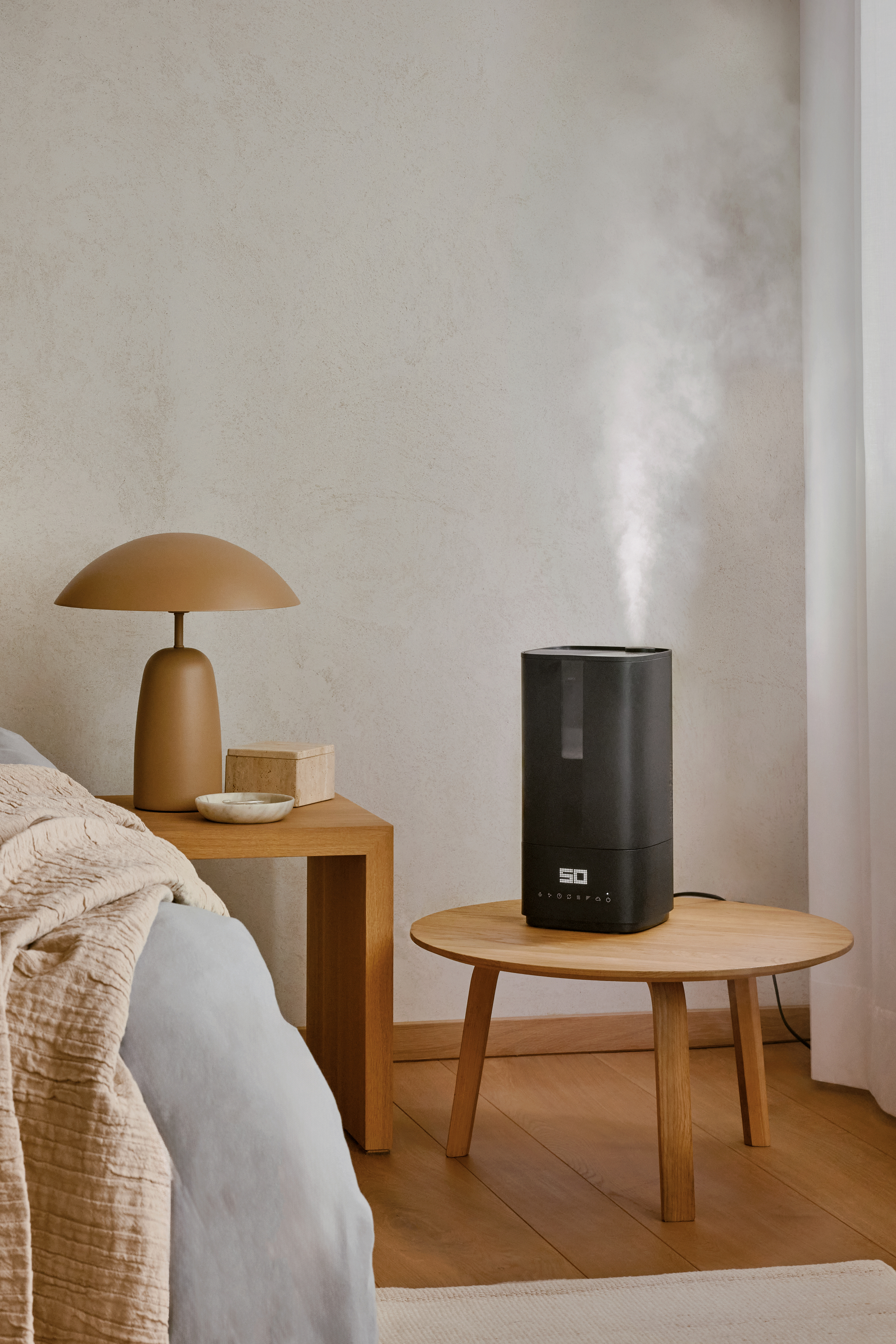 A bedroom scene features a humidifier on a table. A lamp, a box, and a bed are also present. Neutral tones dominate.