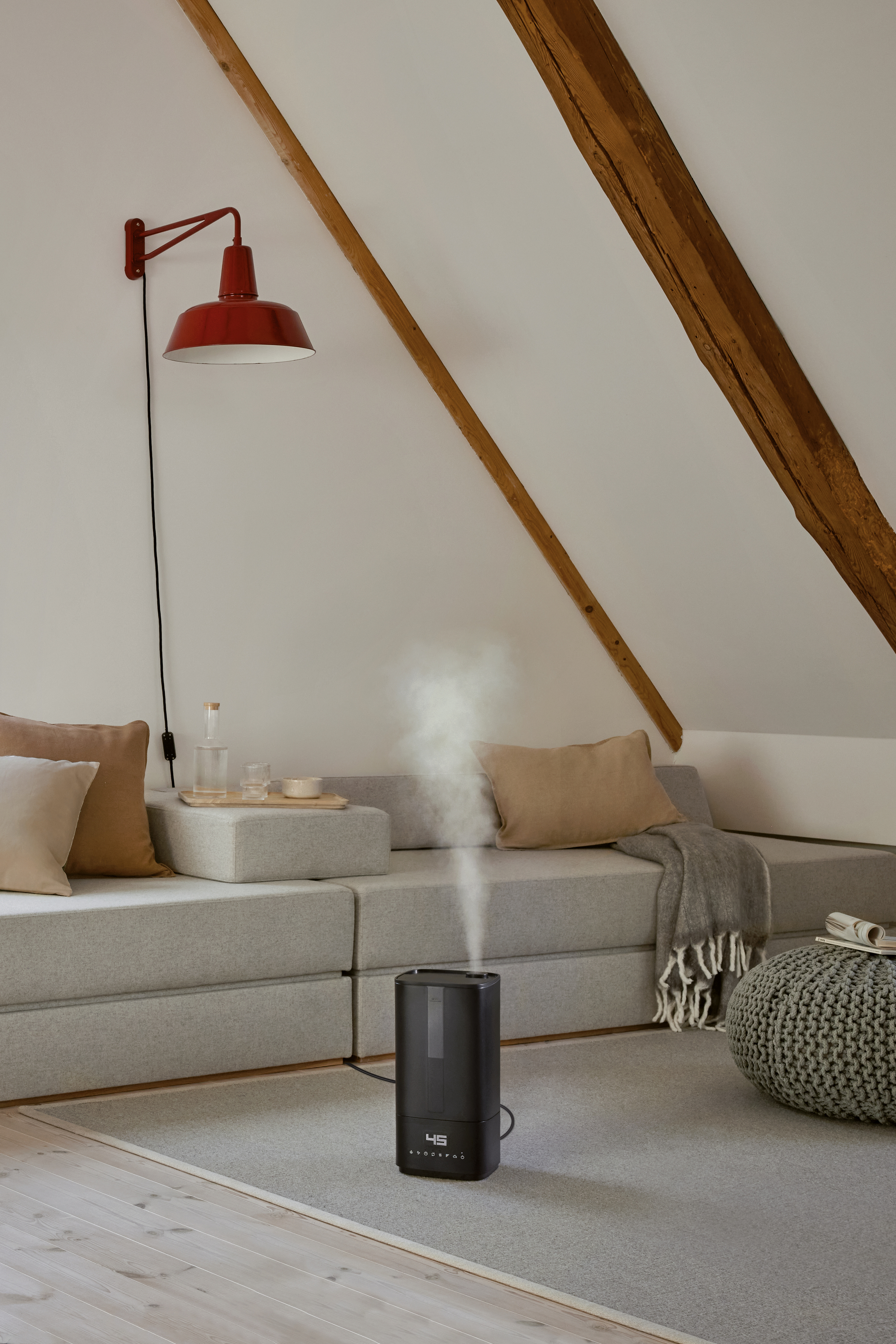 An attic room with a red lamp, gray couch, and a humidifier emitting steam. Wooden beams are visible.