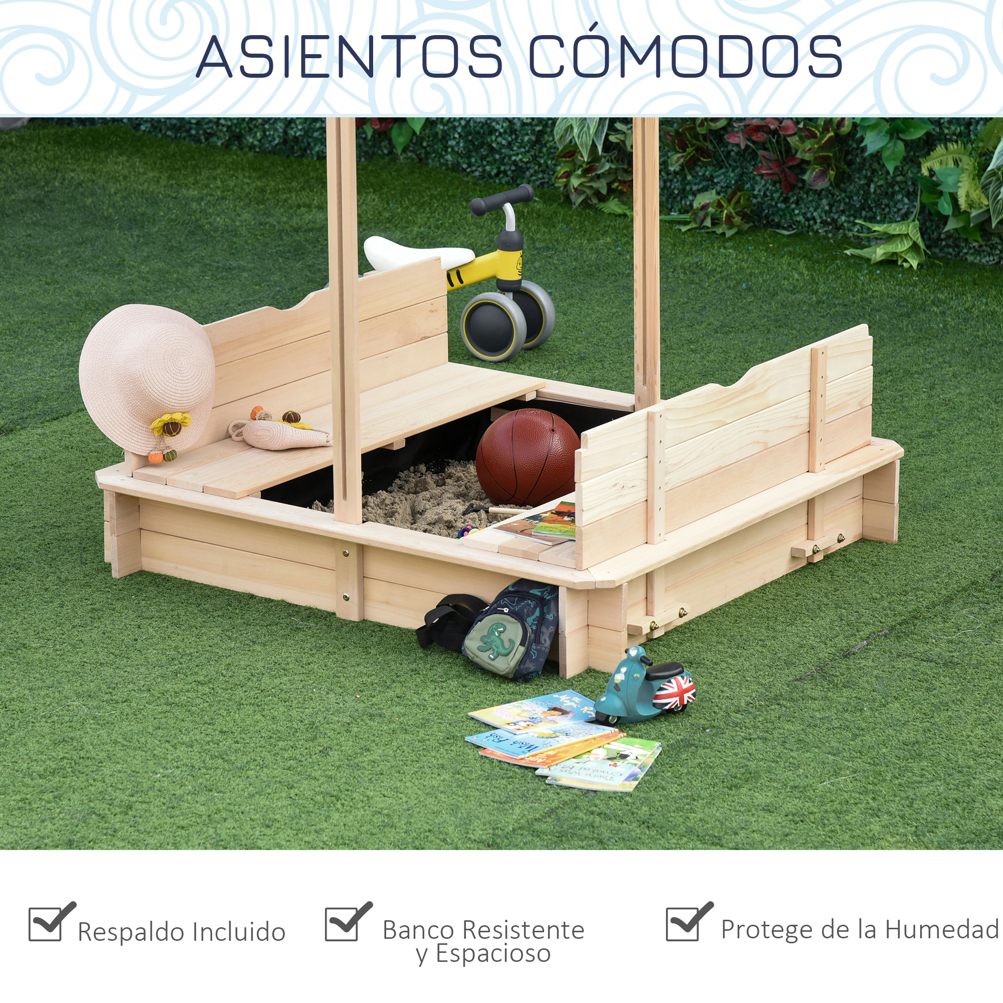 Arenero de madera con juguetes, una bicicleta amarilla y libros sobre hierba verde. Un sombrero y un balón de baloncesto son visibles.