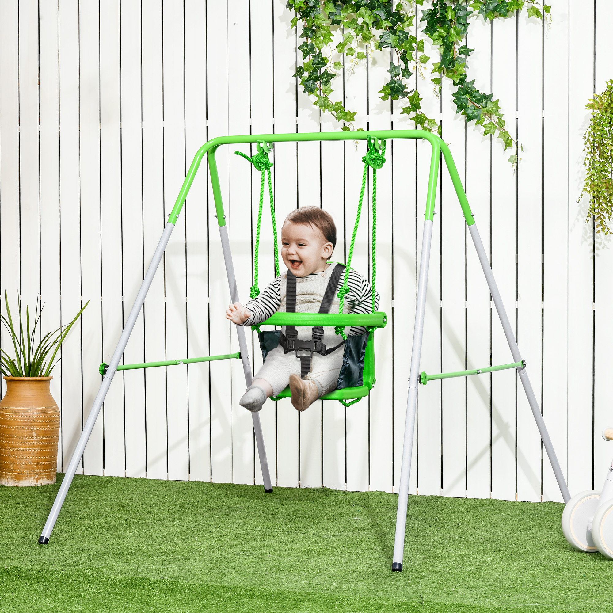 Un bebé feliz en un columpio verde sobre un césped verde. Una valla blanca y enredaderas en el fondo.