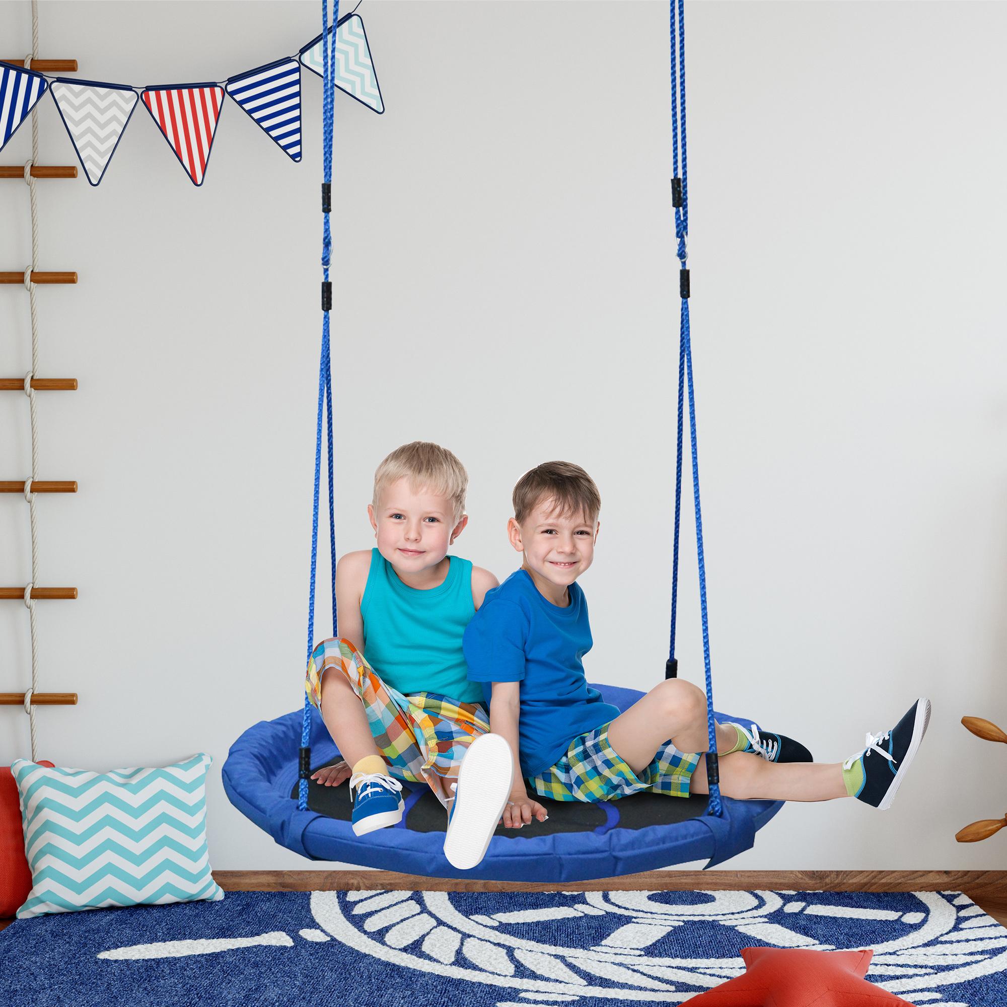 Dos niños se sientan en un columpio azul. La habitación tiene temática náutica con alfombra y decoraciones.