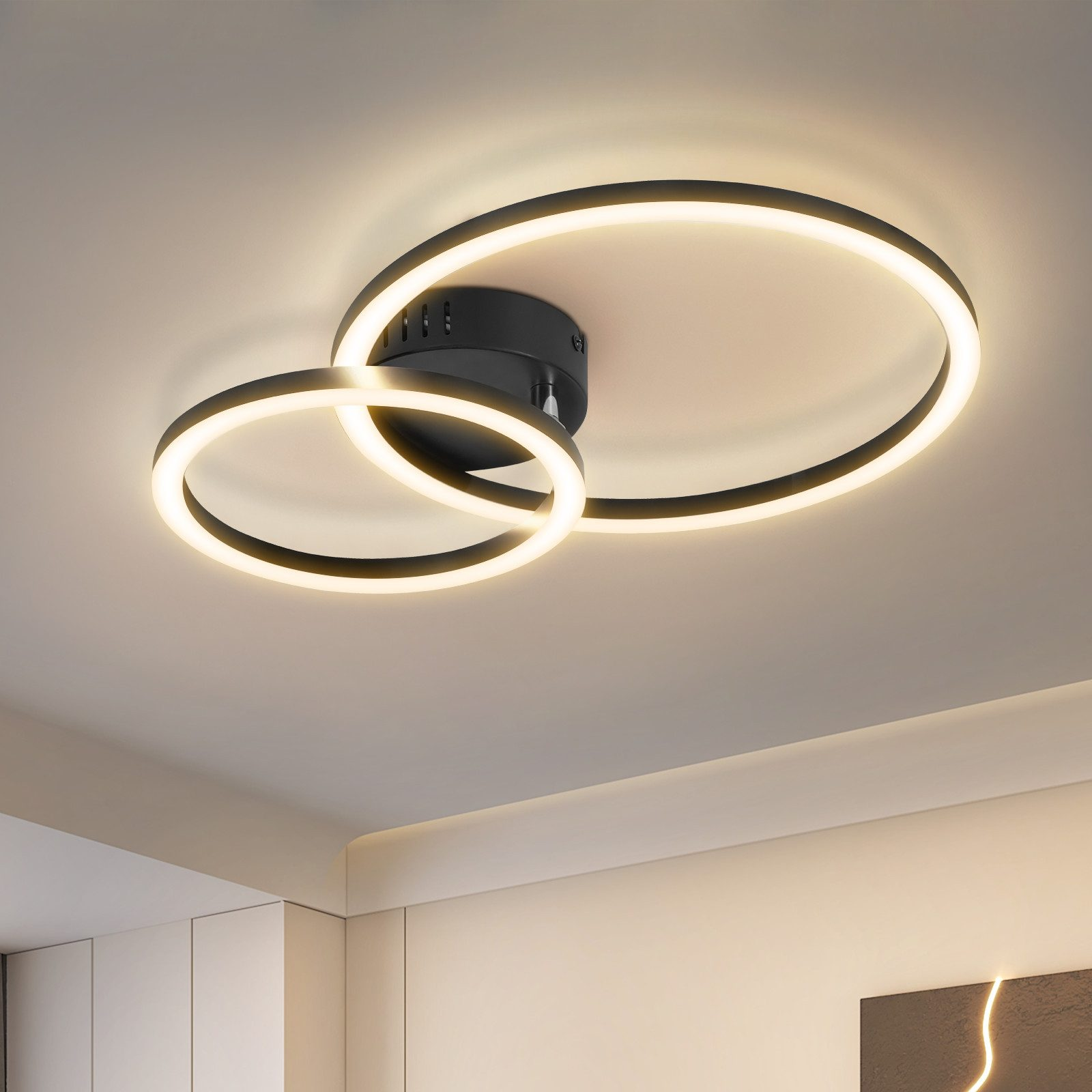 Lampada da soffitto moderna con due anelli intersecanti, che emettono un bagliore caldo contro il soffitto bianco.