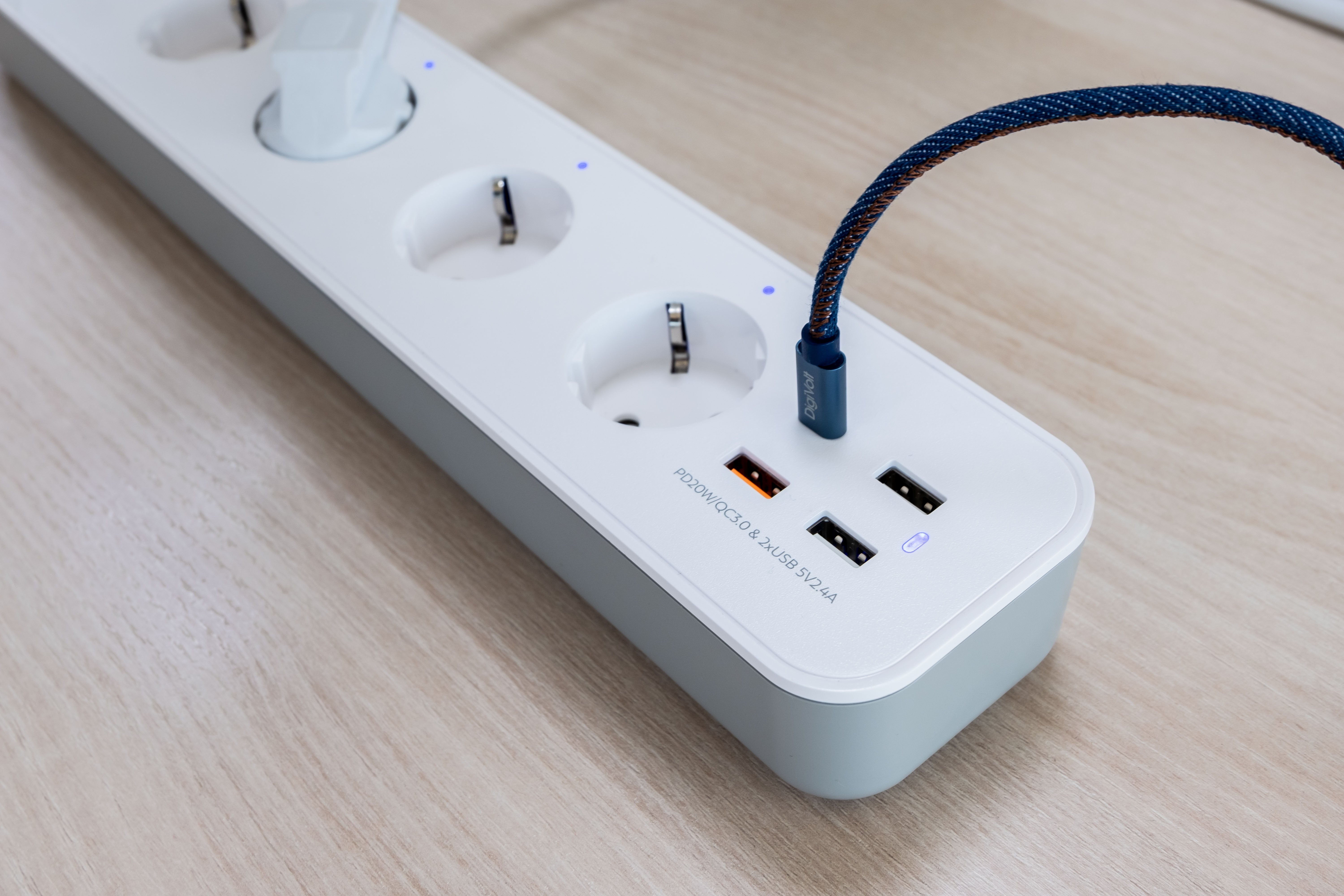Toma en ángulo de una regleta blanca con cable azul y marrón enchufado. La regleta tiene enchufes y puertos USB.