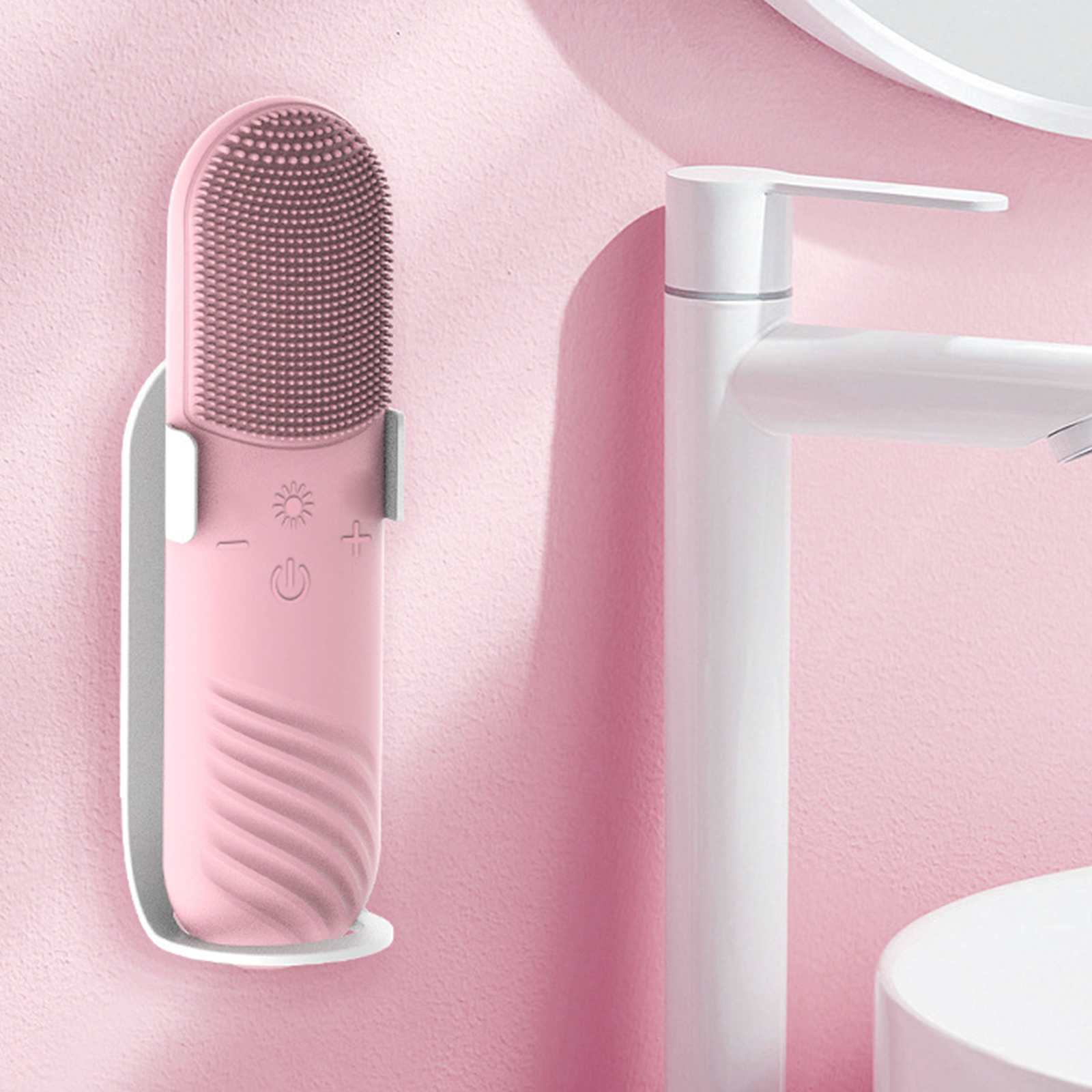 Eine rosa Gesichtsreinigungsbürste in einem weißen Halter neben einem weißen Wasserhahn vor einer rosa strukturierten Wand.