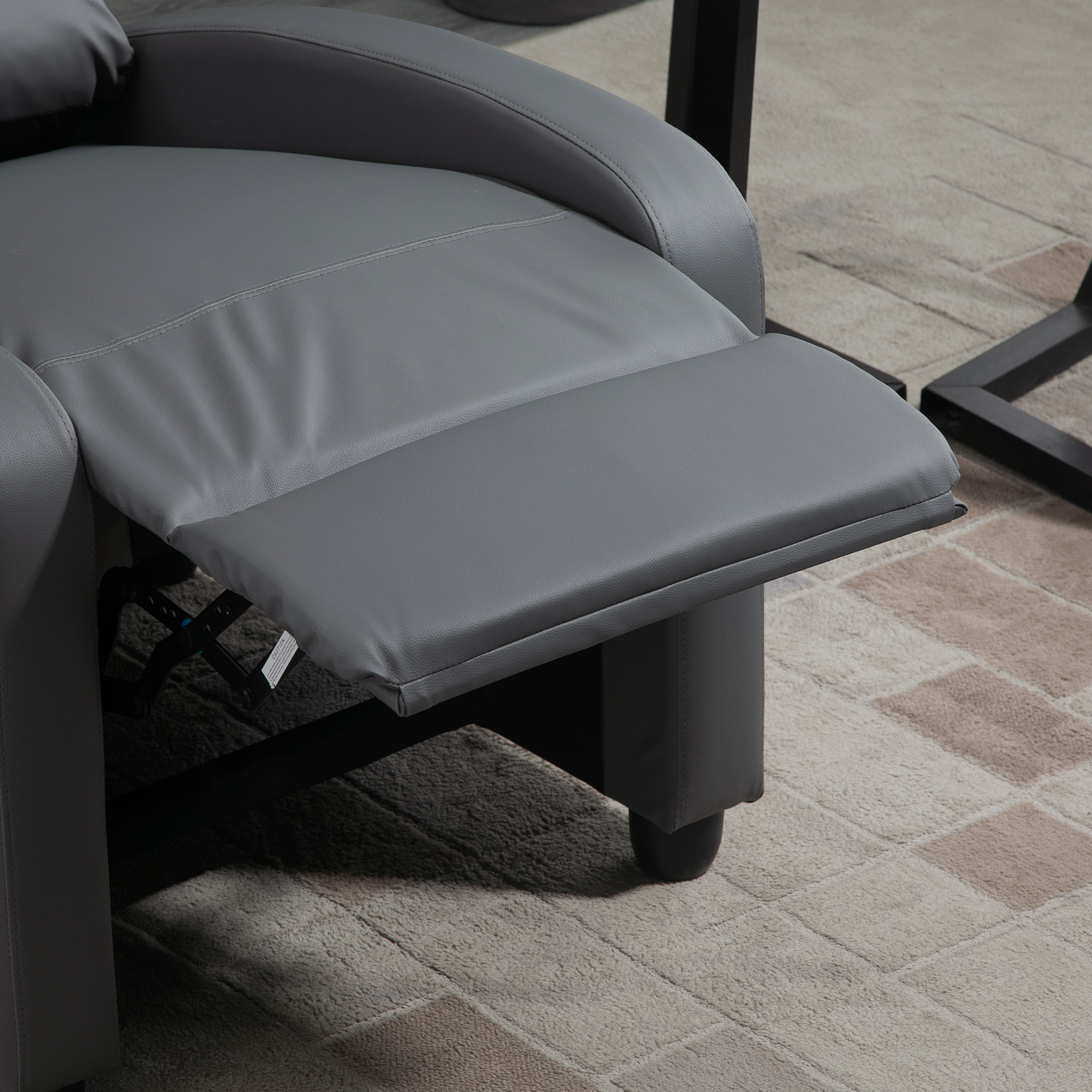 Un sillón reclinable gris con el reposapiés extendido. Está sobre una alfombra estampada. Parte de una mesa negra es visible.