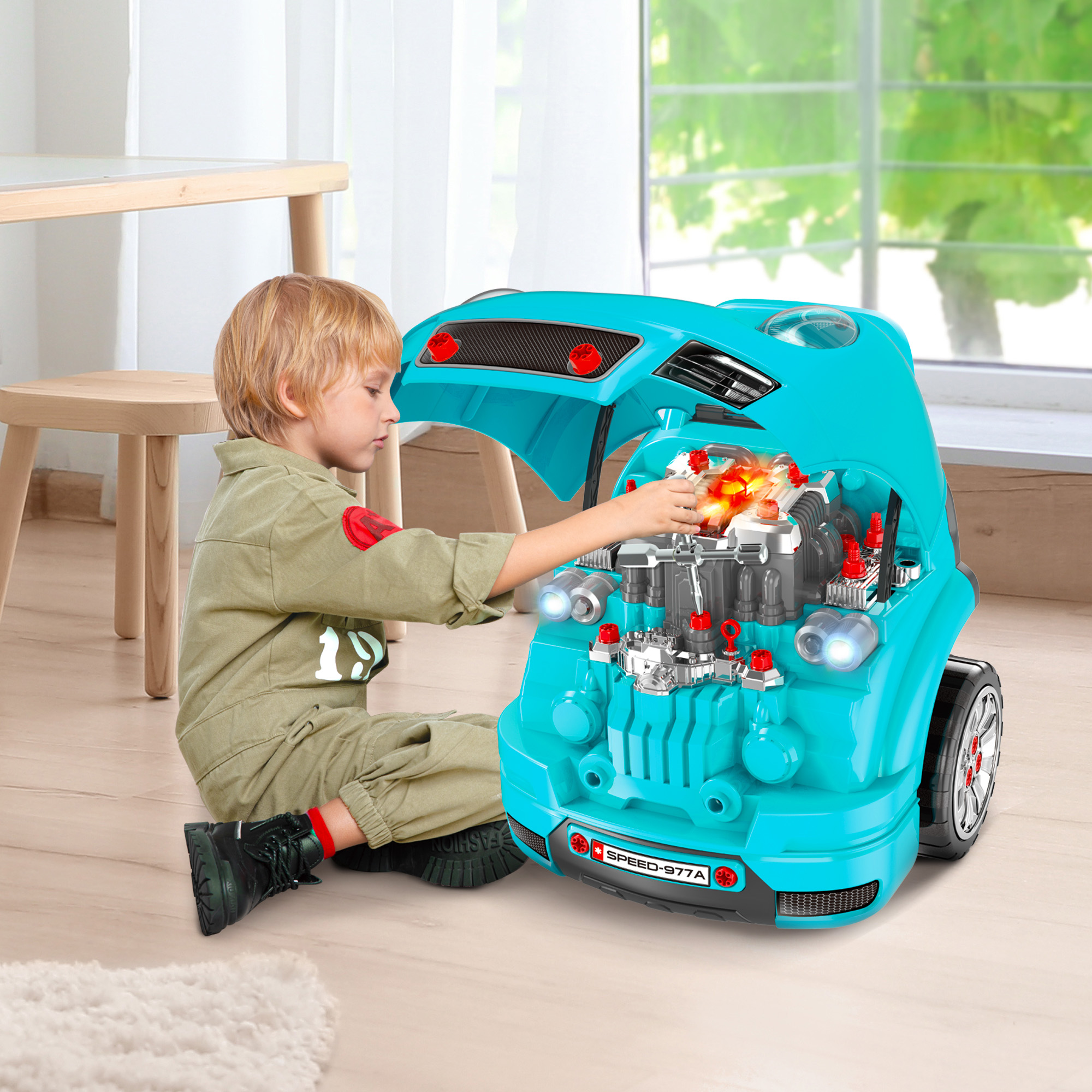 Un niño pequeño con un mono juega con un coche de juguete azul con el capó abierto, revelando el motor.