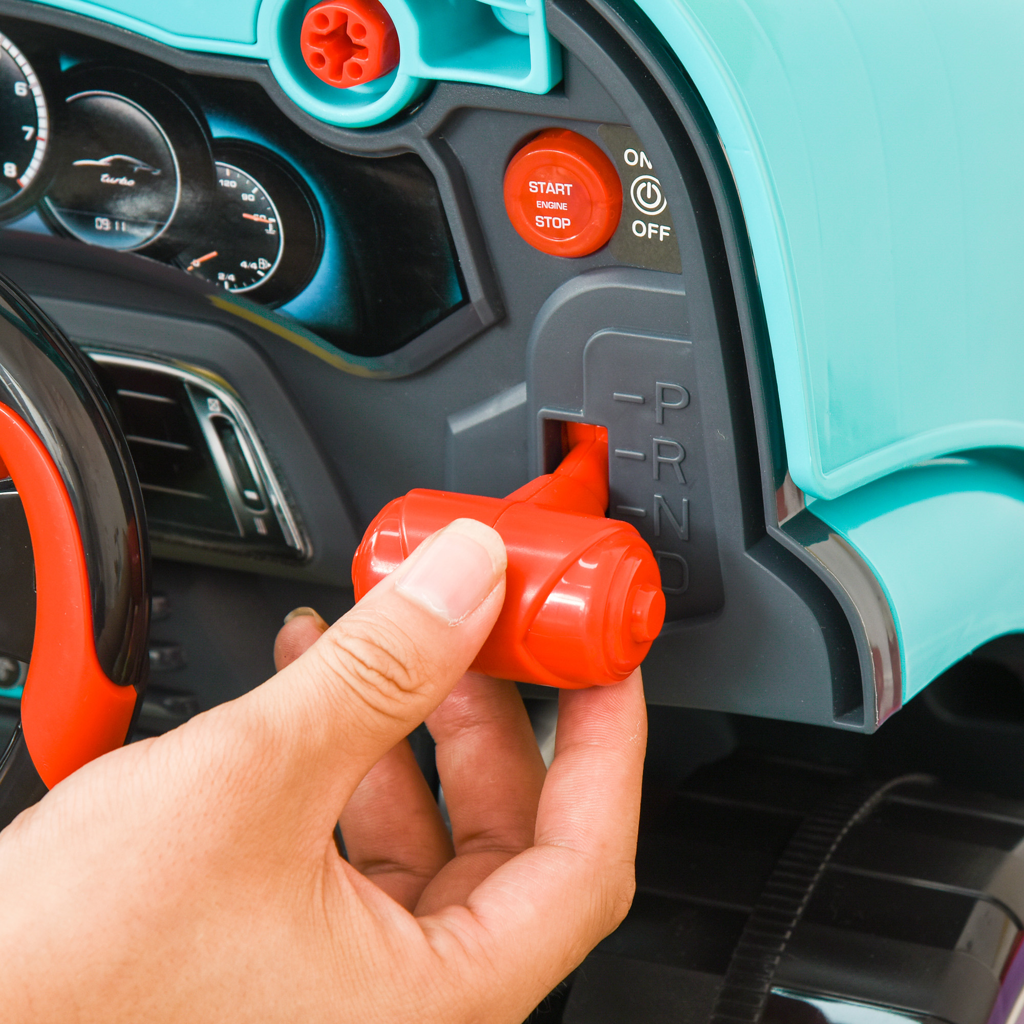Una mano ajusta una palanca de cambios roja en un coche de juguete. Detalles del salpicadero, incluidos indicadores y botón de arranque/parada, son visibles.