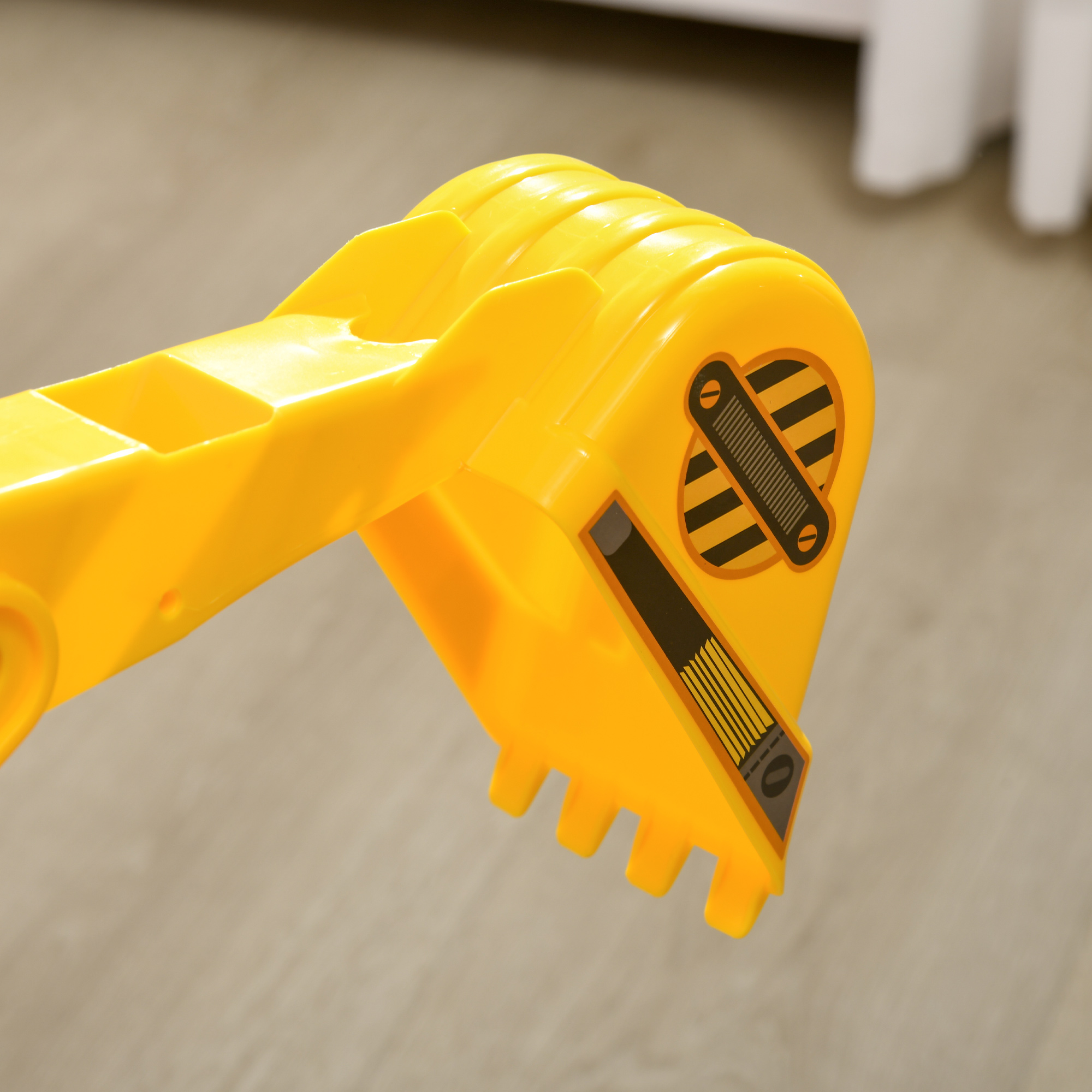 Primer plano de un cubo de excavadora de juguete amarillo. Tiene rayas negras y está sobre una superficie marrón claro.