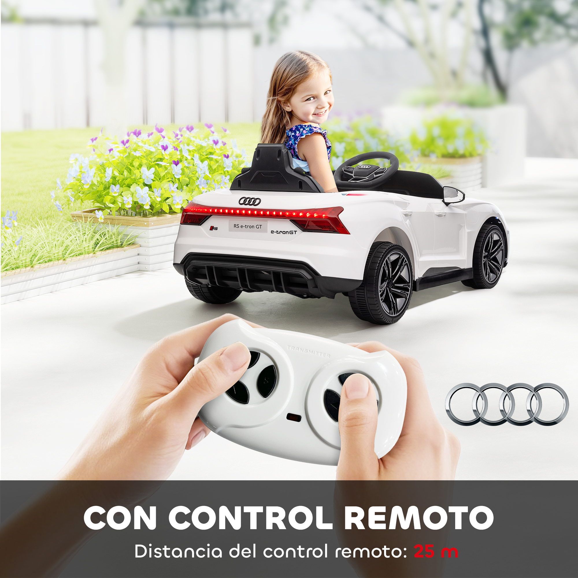 Una niña sonríe en un coche de juguete blanco. Una persona sostiene un mando a distancia. Flores y el logo de Audi en el fondo.