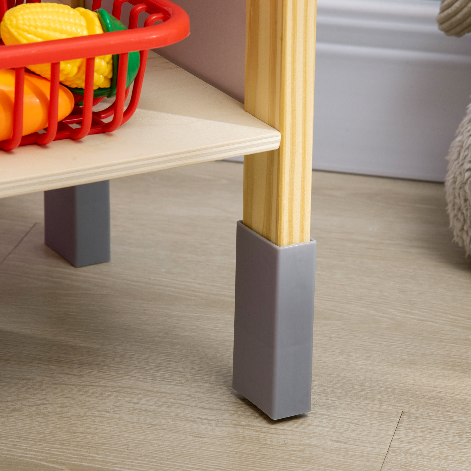 Una mesa de juguete de madera con verduras de juguete en una cesta roja. Protectores de patas grises en las patas de la mesa.