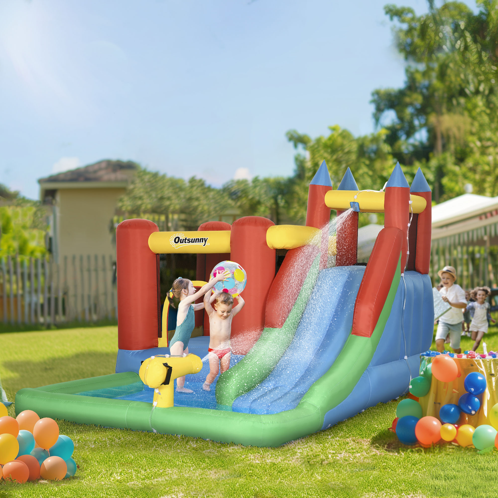 Los niños juegan en un tobogán acuático y una casa inflable. Una pistola de agua rocía agua. Globos en primer plano.