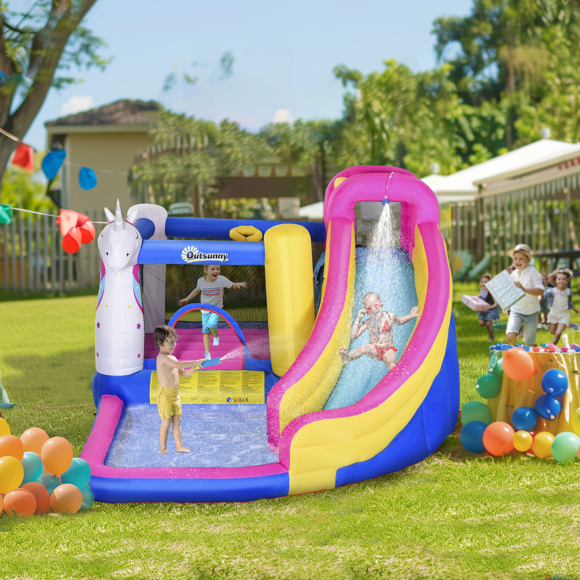 Niños jugando en un parque acuático inflable colorido con tobogán y diseño de unicornio. Otros niños jugando afuera.