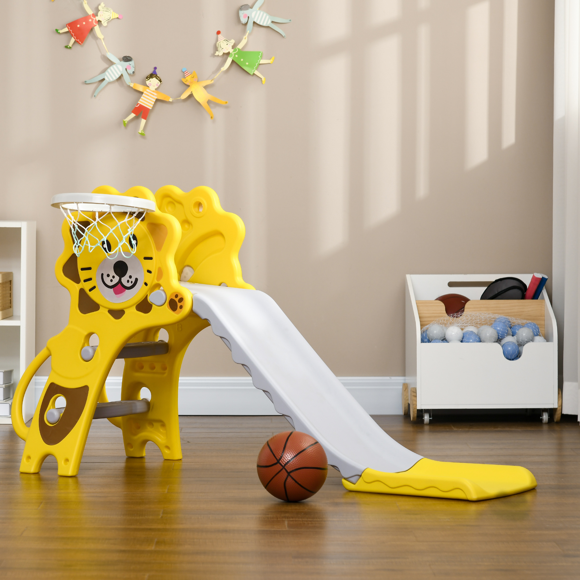 Un tobogán amarillo con cara de león con aro de baloncesto, un baloncesto y figuras de juguete. La escena es en una habitación.